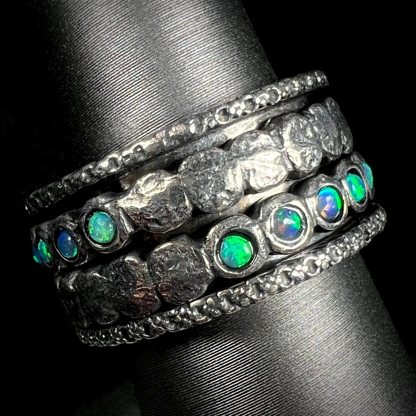 A sterling silver opal spinner ring for men with a hammered texture, shown at an angle against a black backdrop.
