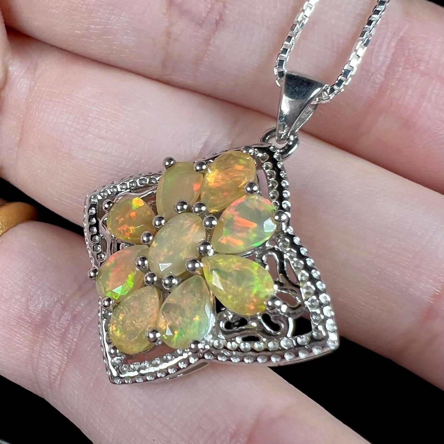 A sterling silver opal star necklace shown in a hand at an angled view.  The opals have red and green color play.