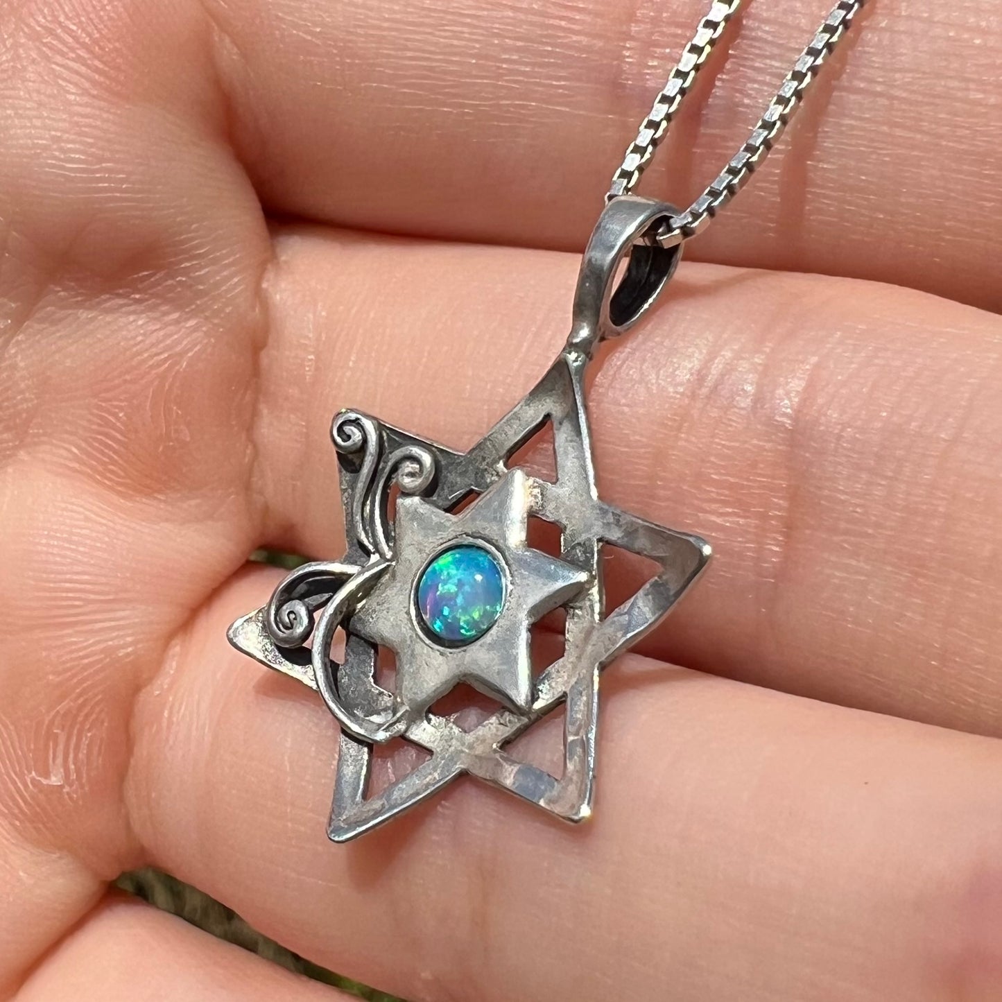 Close-up angled daylight view of a silver Star of David necklace set with a round blue lab-created opal.