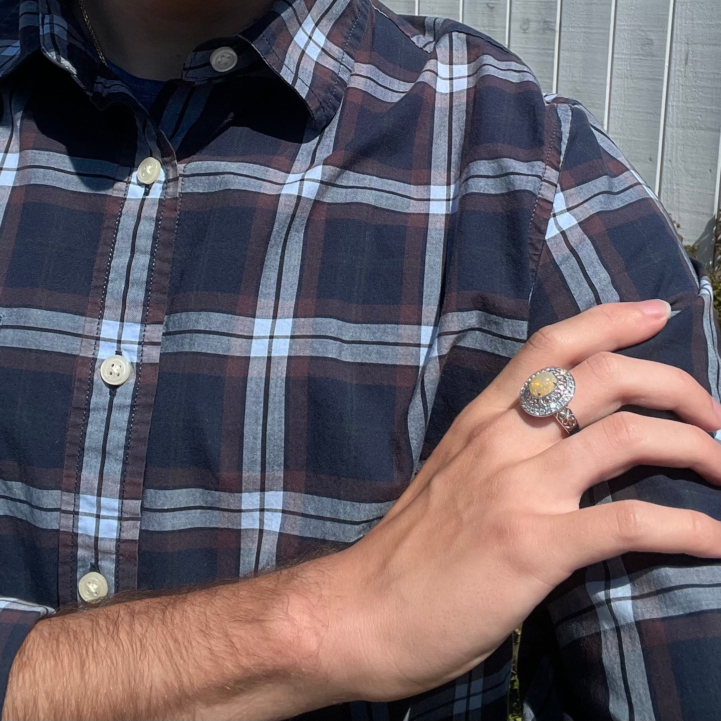 Silver Ethiopian opal statement ring worn on a hand against a model's blue plaid shirt.