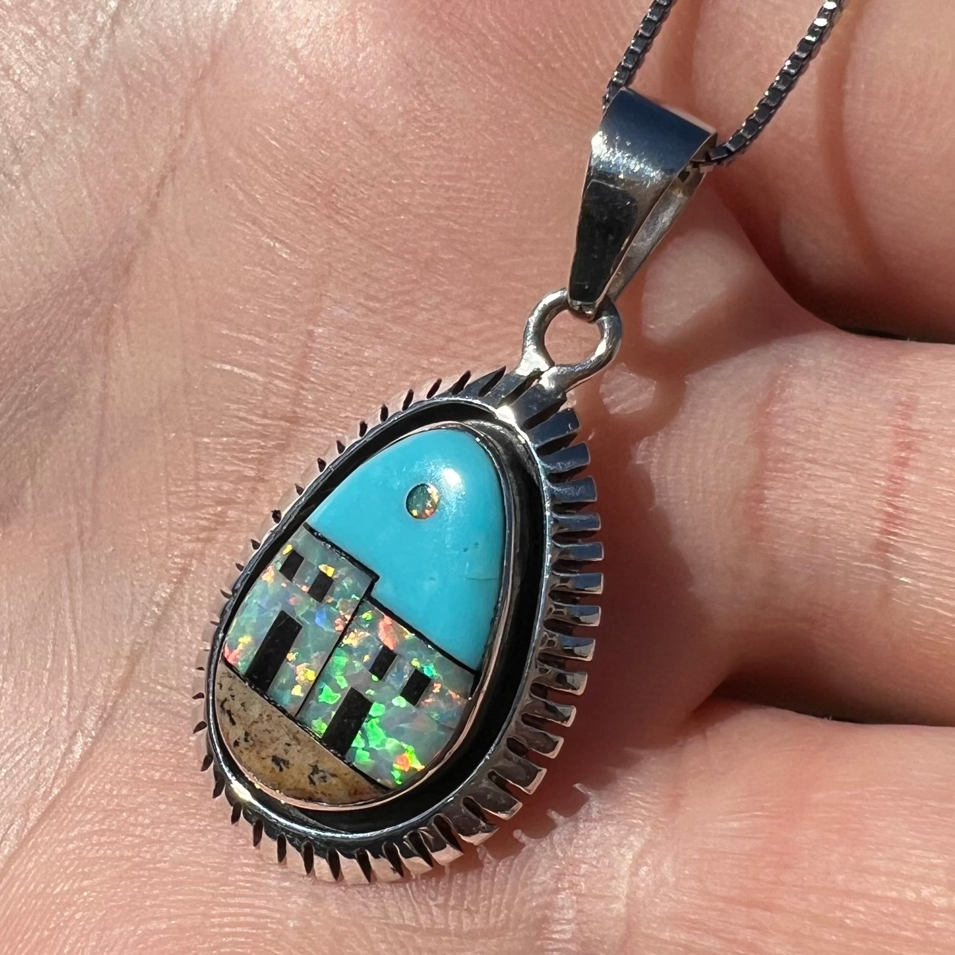 A Southwest-style silver opal and turquoise inlay necklace, shown in a hand at an angle in sunlight.
