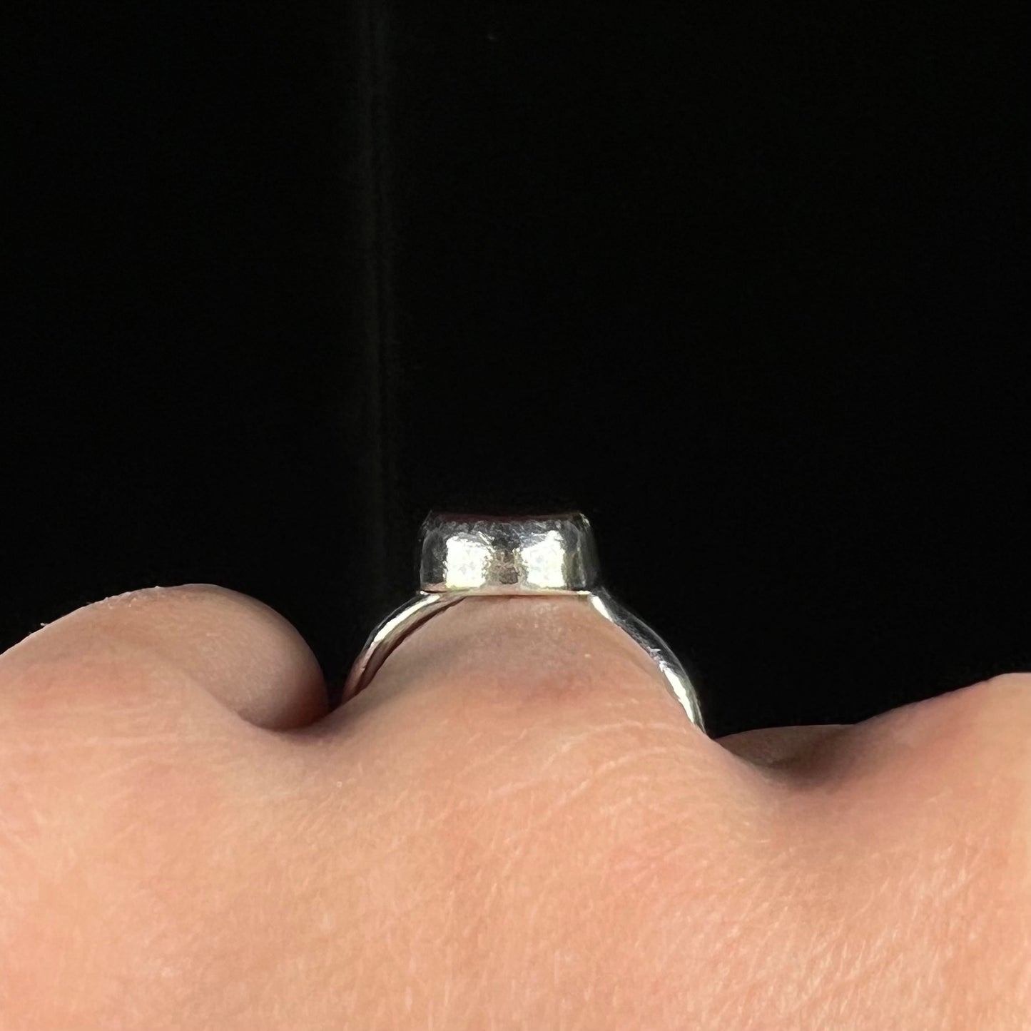 Side gallery profile view of a silver ring worn on a finger against a dark backdrop.