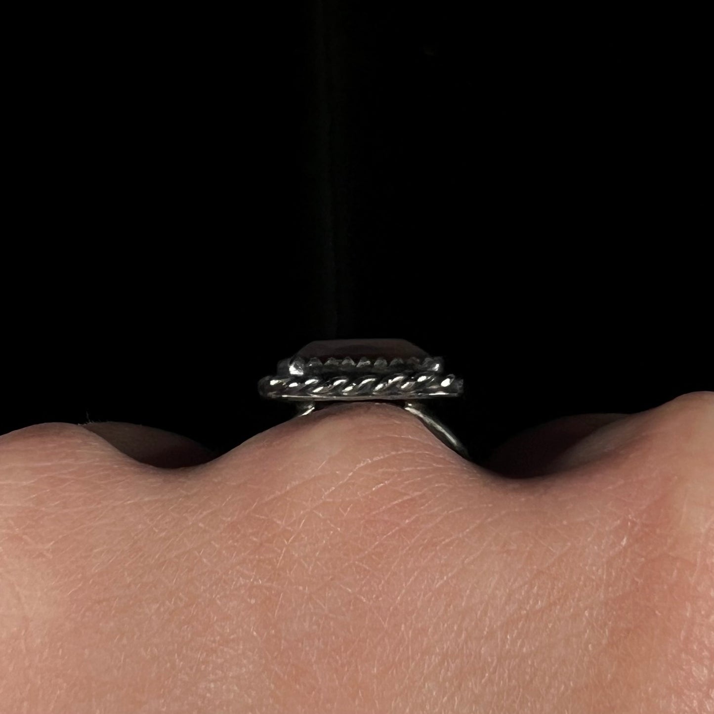 Side gallery view of the silver rope bezel on a fire agate ring, worn on a hand against a dark background.