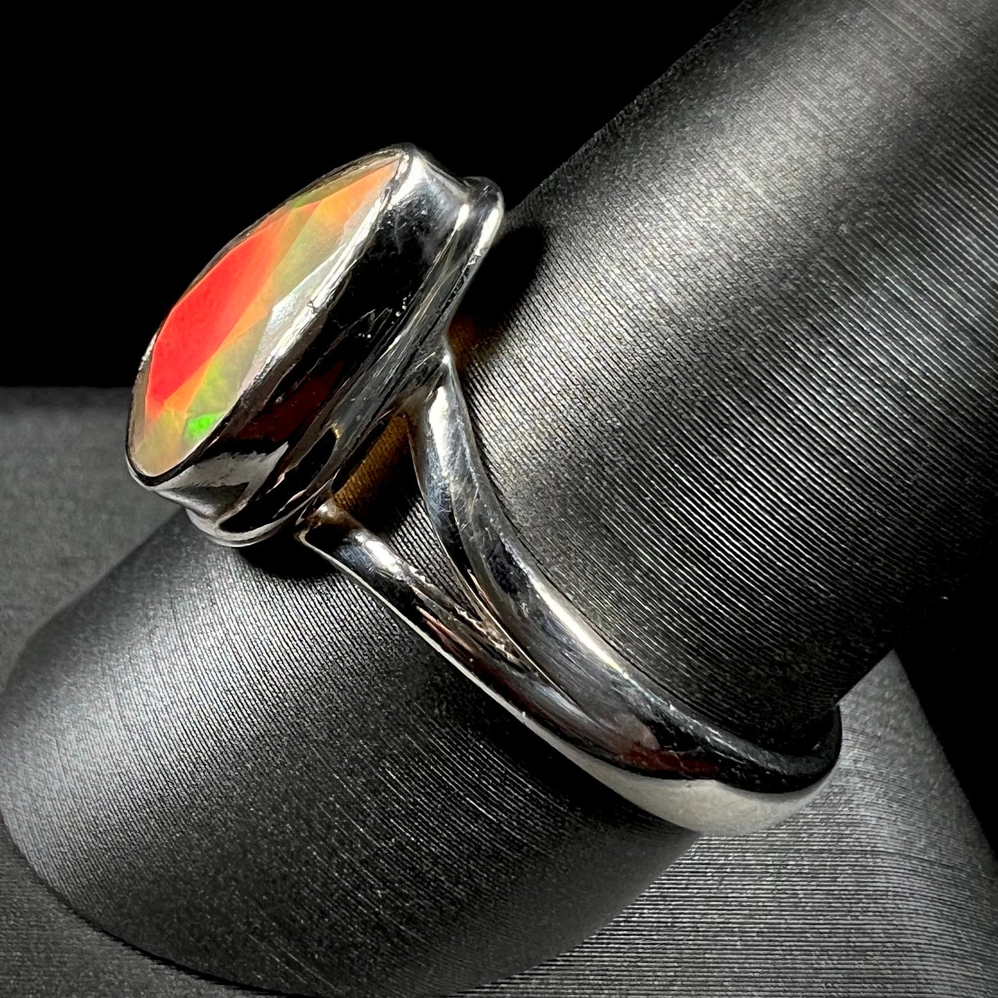 A unisex sterling silver ring set with a faceted pear shaped Ethiopian fire opal. The opal plays orange, red, and green colors.