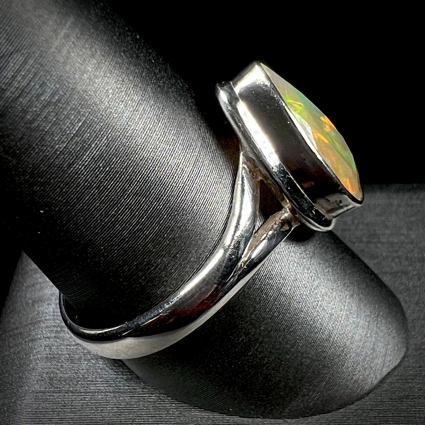 A unisex sterling silver ring set with a faceted pear shaped Ethiopian fire opal. The opal plays orange, red, and green colors.