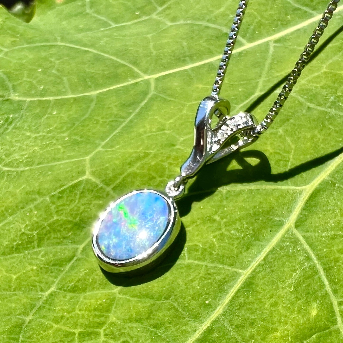 An oval cut black opal doublet necklace set in sterling silver with white zircon accent stones.