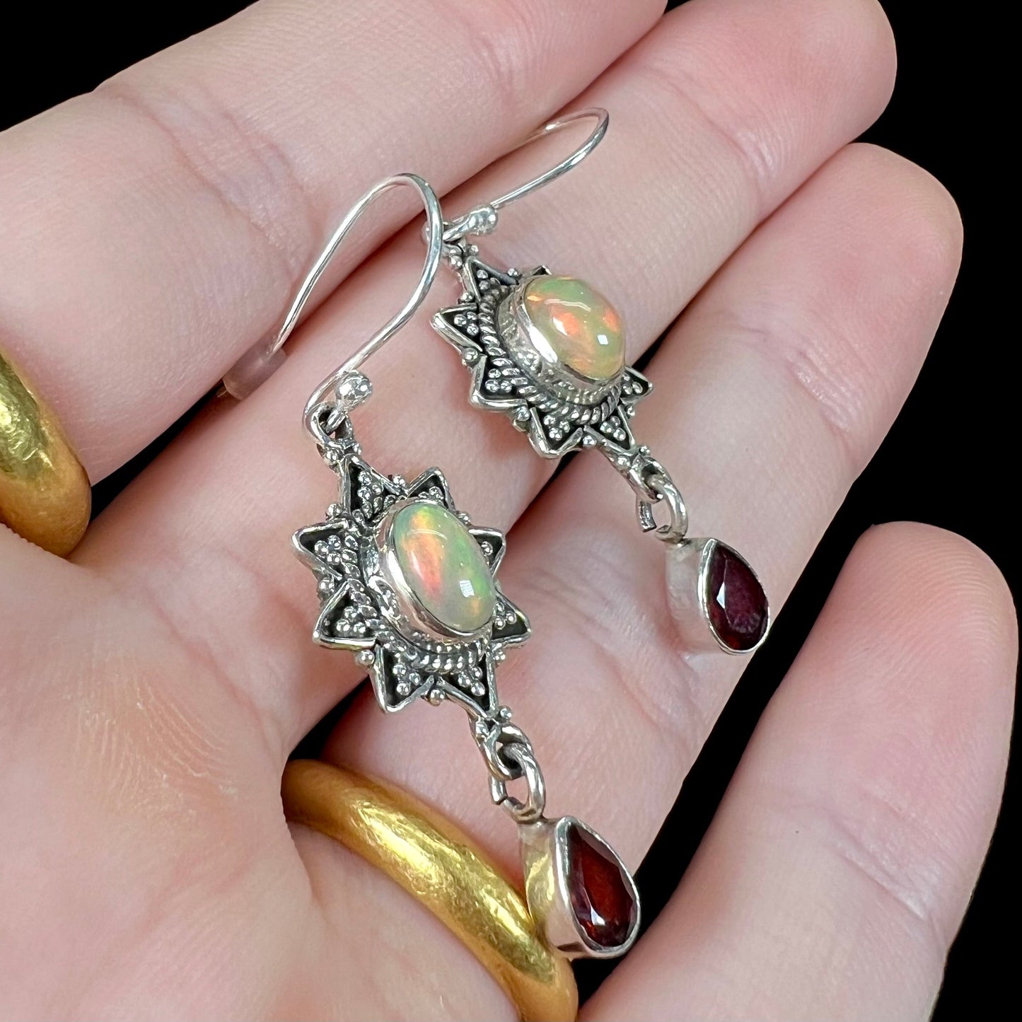 A pair of sterling silver star design dangle earrings set with Ethiopian fire opals and pear shaped red garnet accents.
