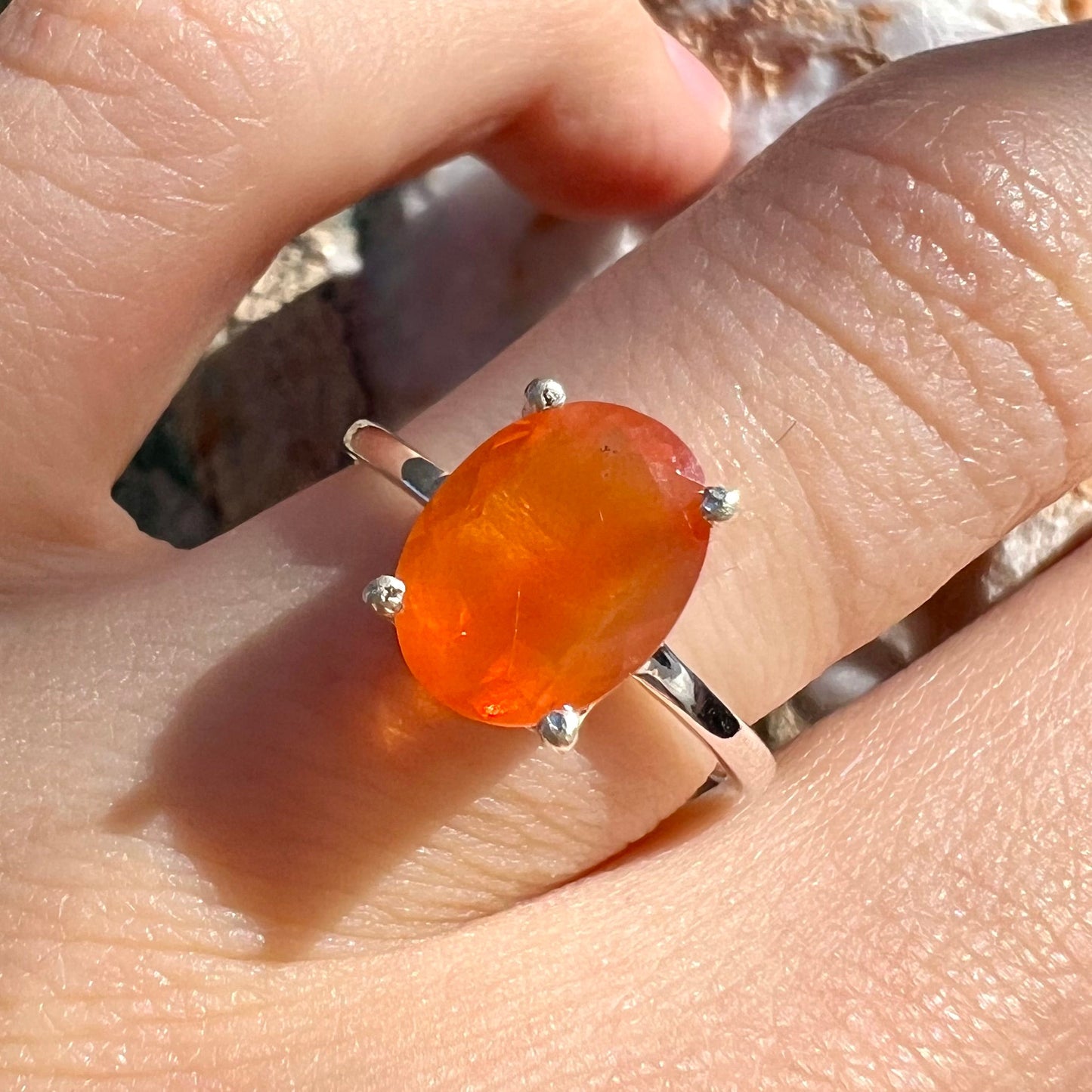 A silver solitaire ring set with a natural, faceted oval cut Mexican fire opal. The stone is a bright orange color.