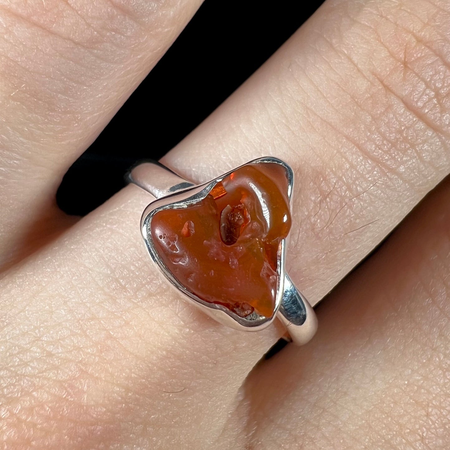 A polished fire opal crystal bezel set into a sterling silver ring. The opal is an orange color.