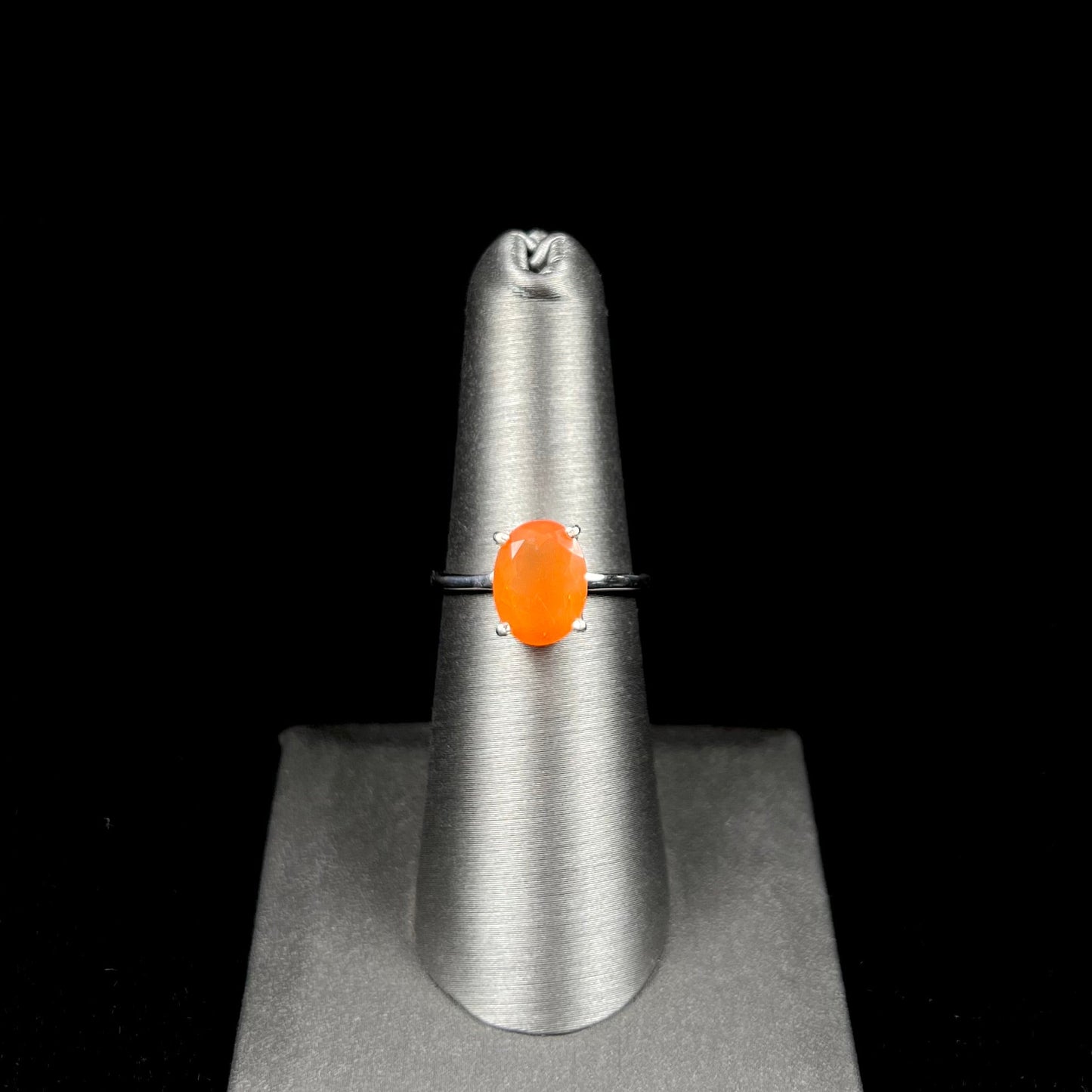 A silver solitaire ring set with a natural, faceted oval cut Mexican fire opal. The stone is a bright orange color.