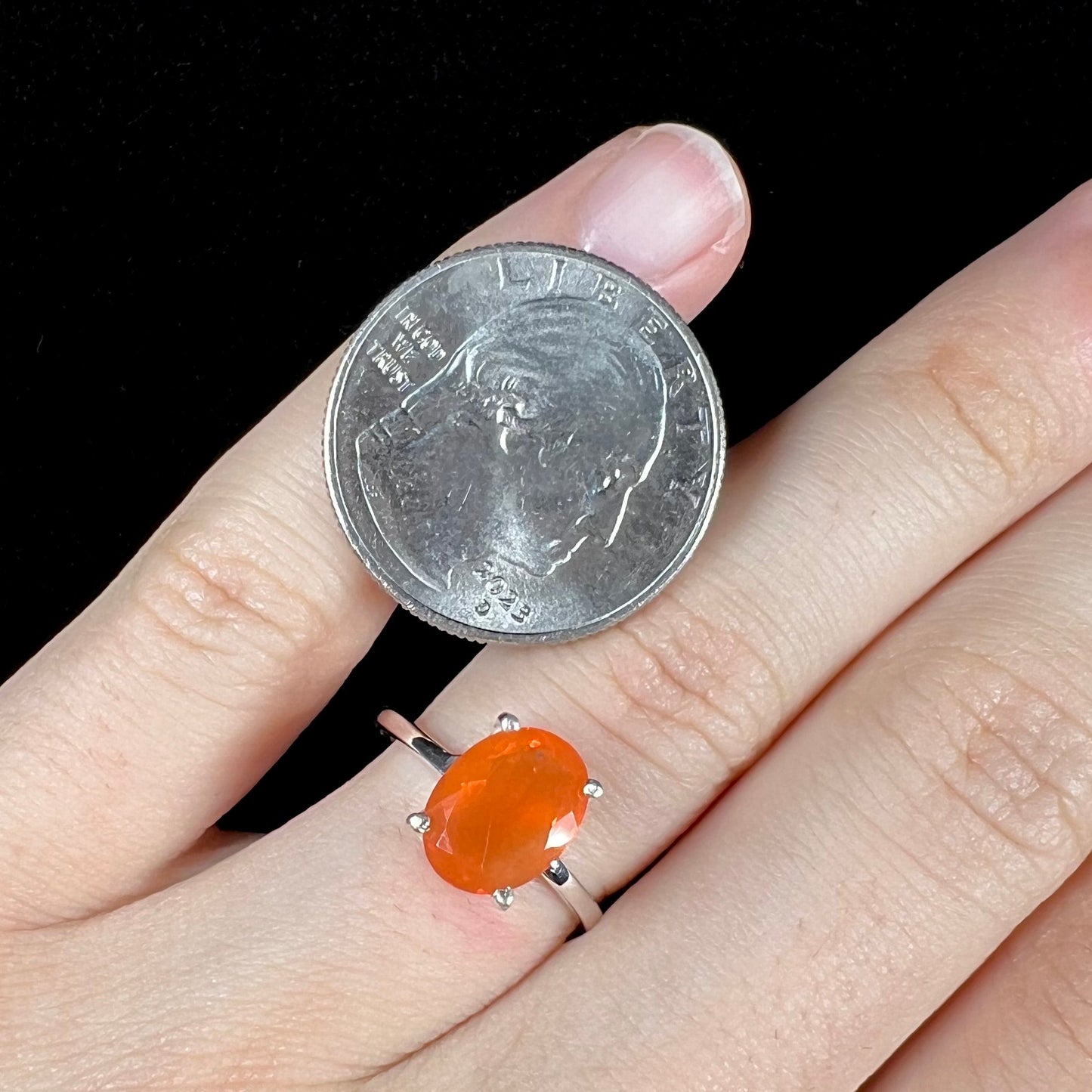 A silver solitaire ring set with a natural, faceted oval cut Mexican fire opal. The stone is a bright orange color.