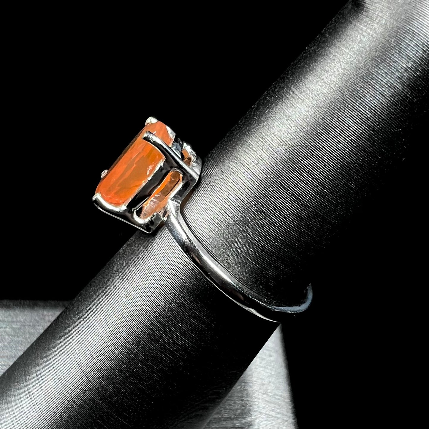A silver solitaire ring set with a natural, faceted oval cut Mexican fire opal. The stone is a bright orange color.