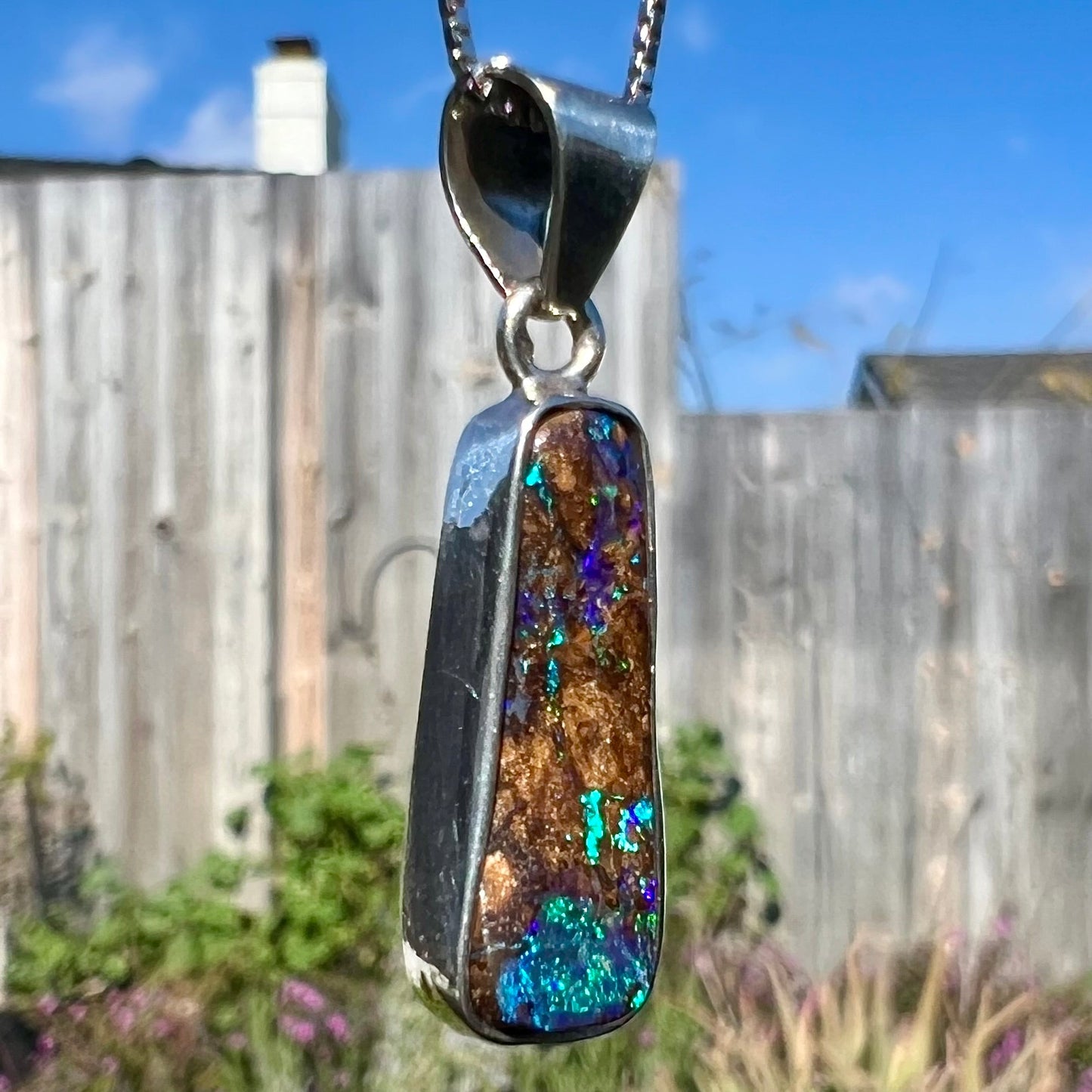 An elongated shaped natural boulder opal necklace in sterling silver. The opal flashes bright blue and green colors.