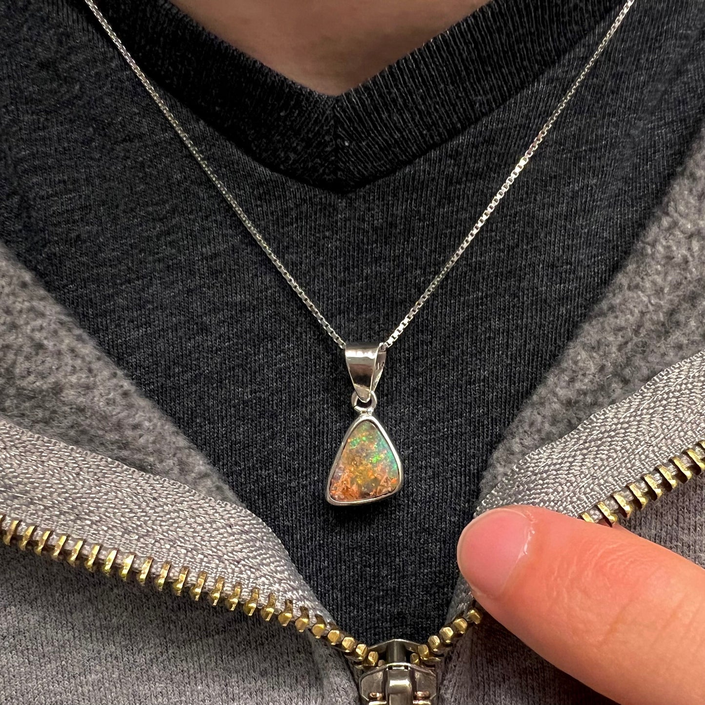 A sterling silver boulder opal necklace on a box chain. The opal twinkles bright red, green, and blue colors.