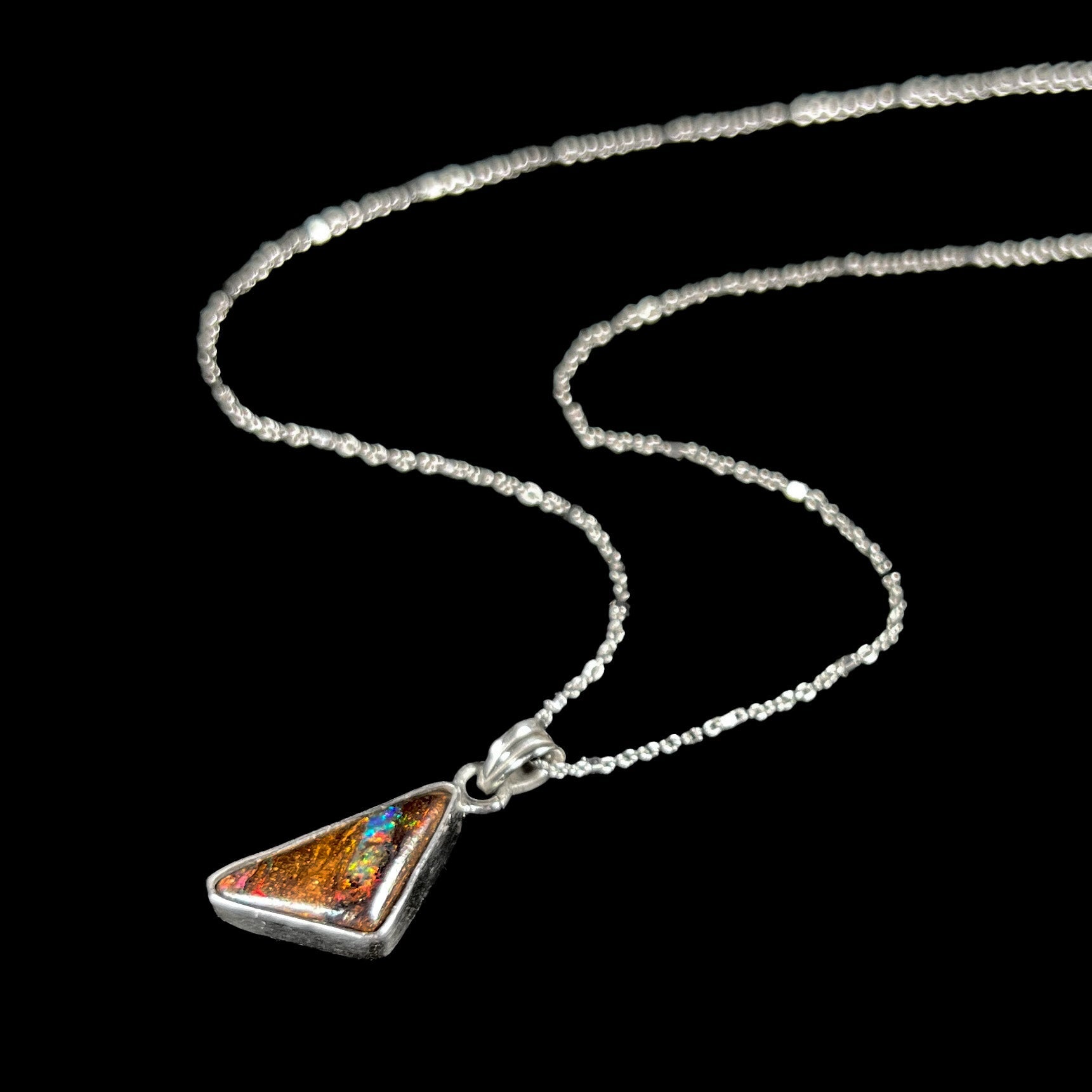 A triangle shaped opal necklace in sterling silver.  The opal shines with every color of the rainbow.