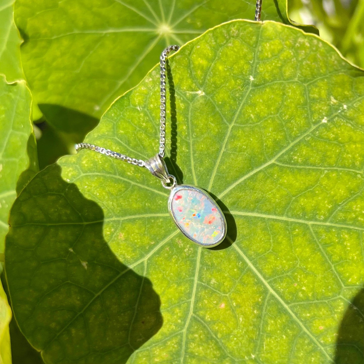 A ladies' sterling silver necklace bezel set with a natural white crystal opal. The opal has red and blue fire.
