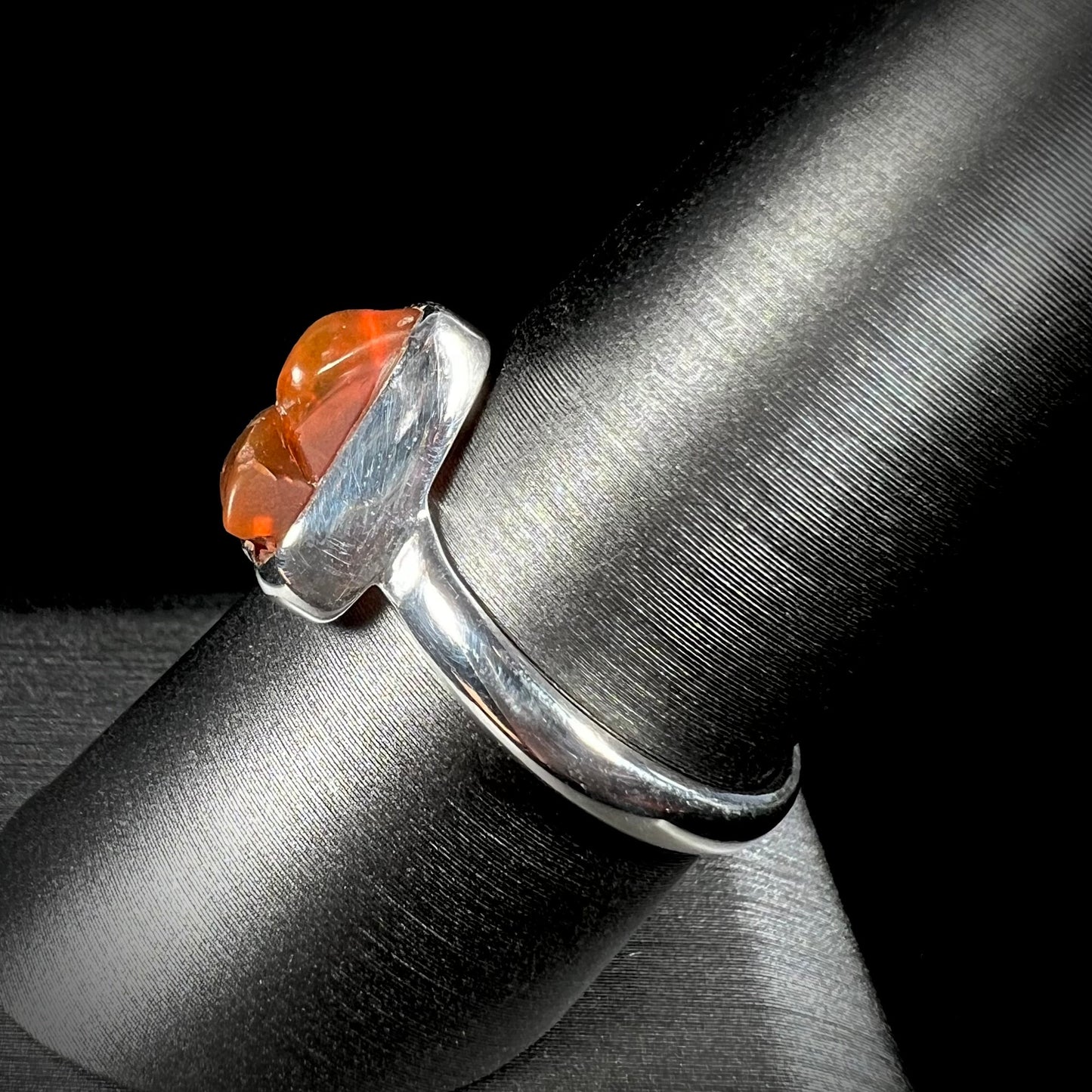 A polished fire opal crystal bezel set into a sterling silver ring. The opal is an orange color.