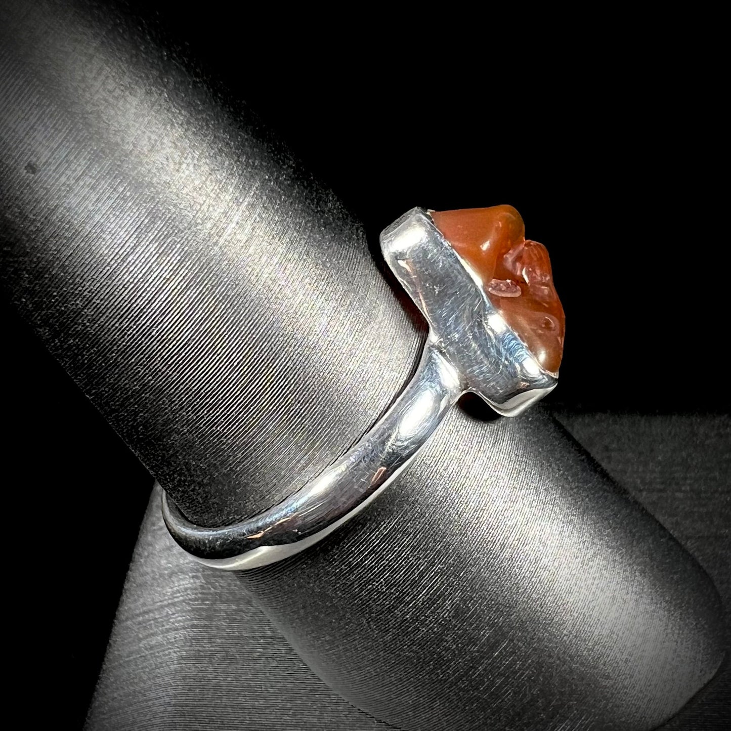 A polished fire opal crystal bezel set into a sterling silver ring. The opal is an orange color.