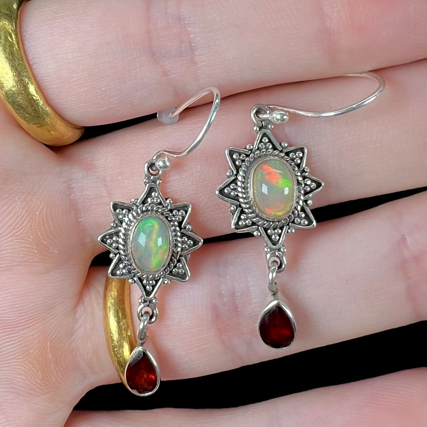A pair of sterling silver star design dangle earrings set with Ethiopian fire opals and pear shaped red garnet accents.