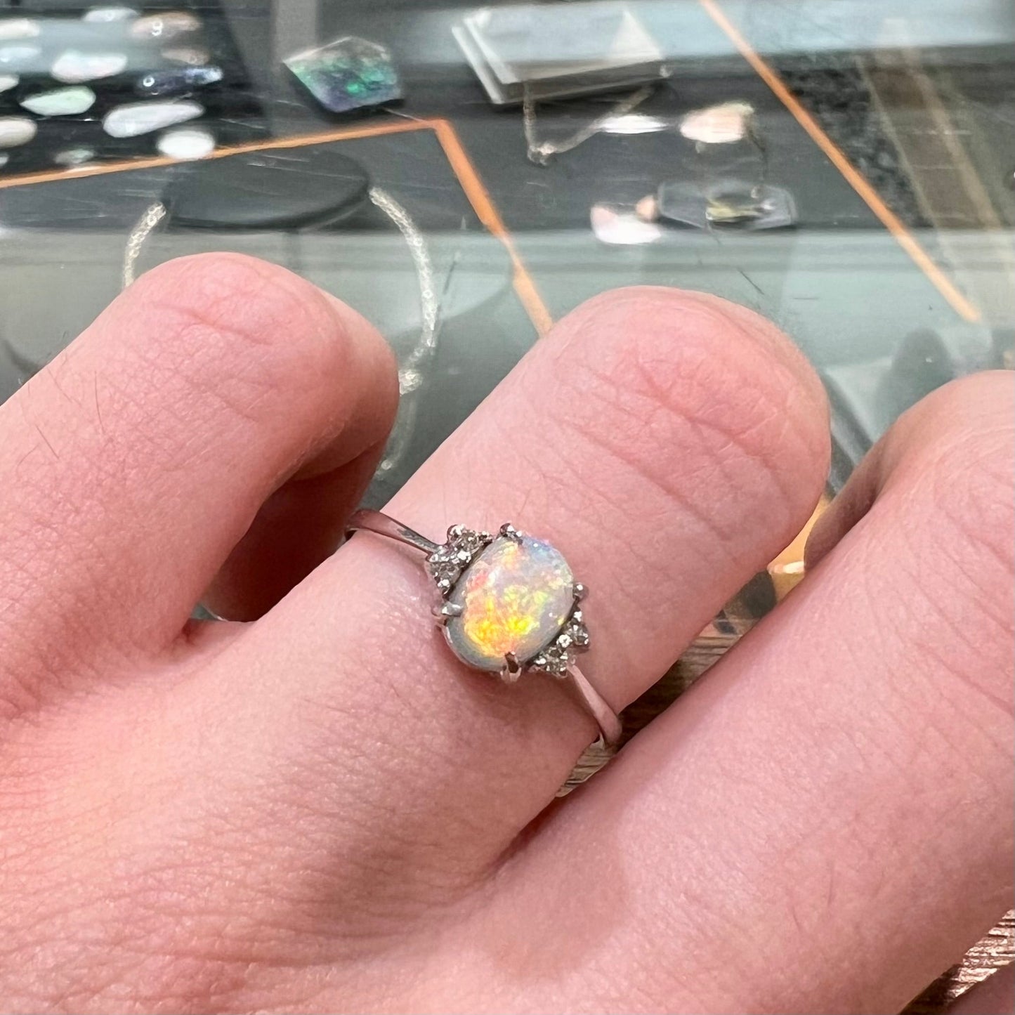 A ladies' white gold opal and diamond ring. The opal shines orange, yellow, and green colors.