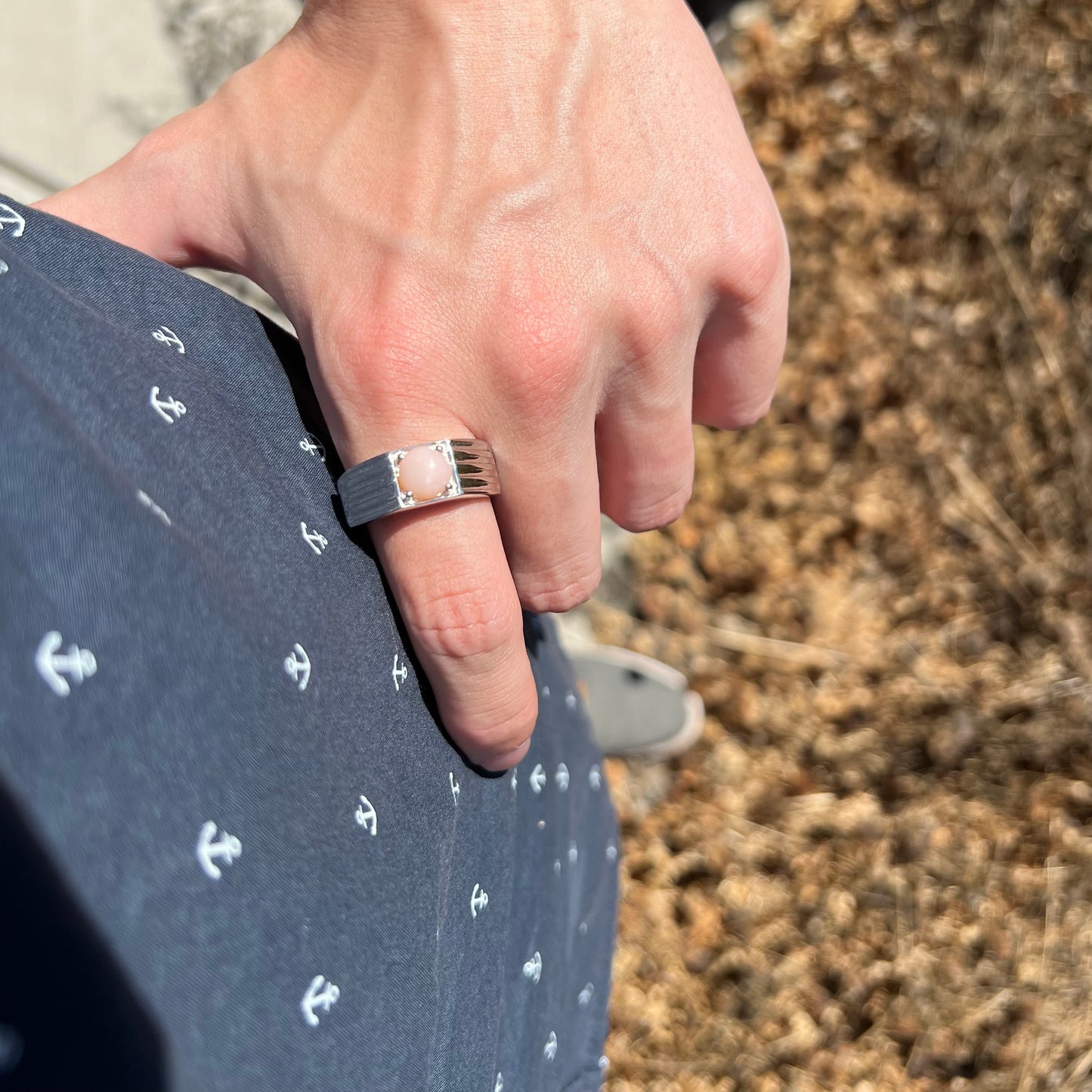 Hand resting on man's hip while wearing sleek sterling silver pink Peruvian opal men's ring in sunlight
