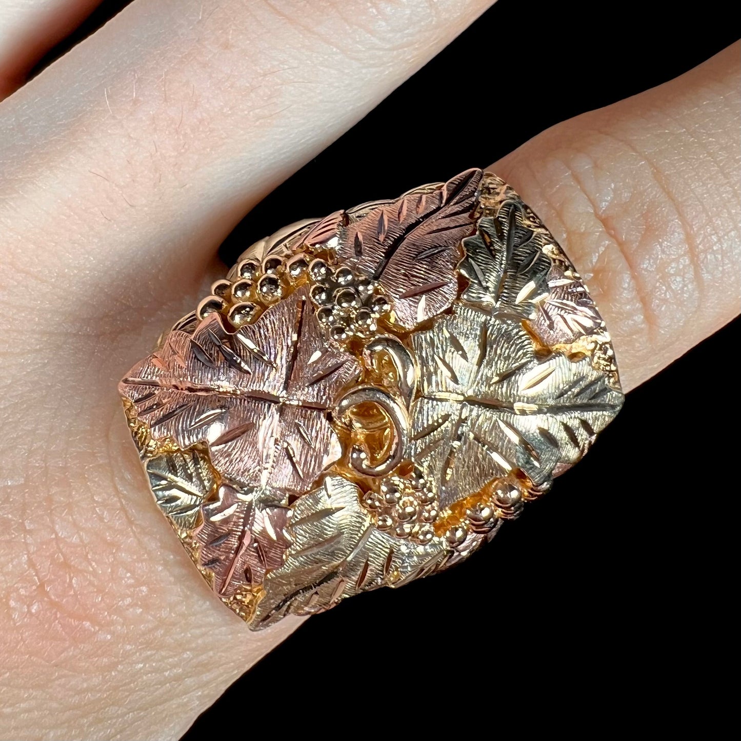 A men's solid gold ring. The ring is Black Hills gold featuring a grapevine and leaf motif with rose and green gold designs.