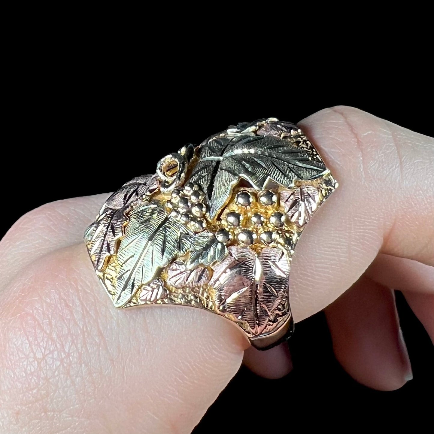 A men's solid gold ring. The ring is Black Hills gold featuring a grapevine and leaf motif with rose and green gold designs.