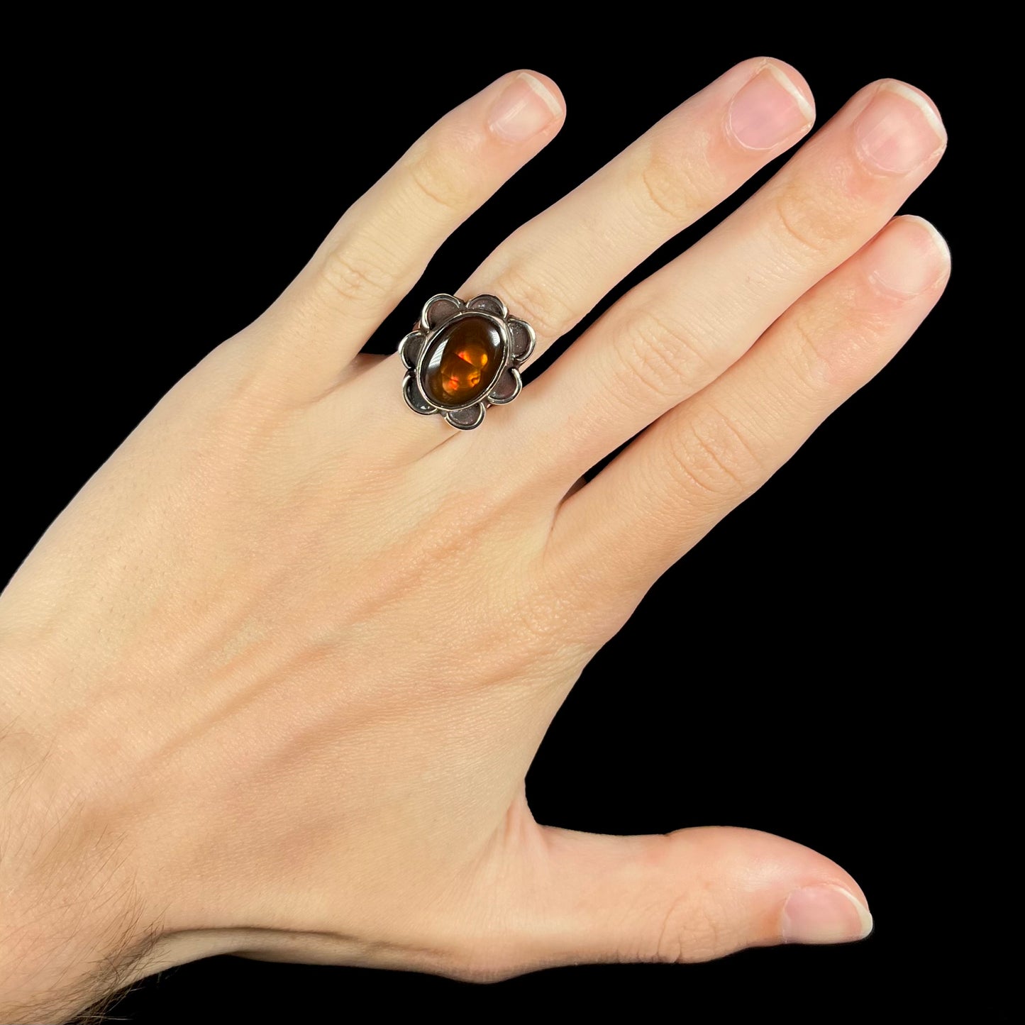 Fire agate ring worn on hand, glowing with orange iridescence.
