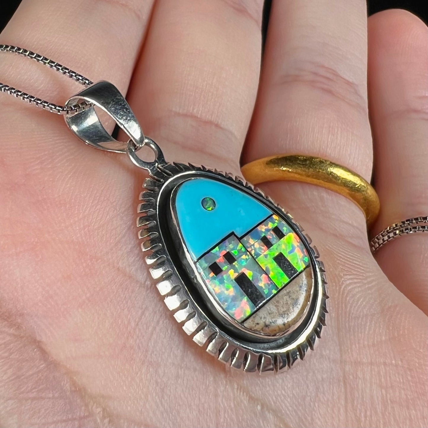 Close-up of a Southwest-style silver opal and turquoise inlay necklace, shown in a hand at an angle.