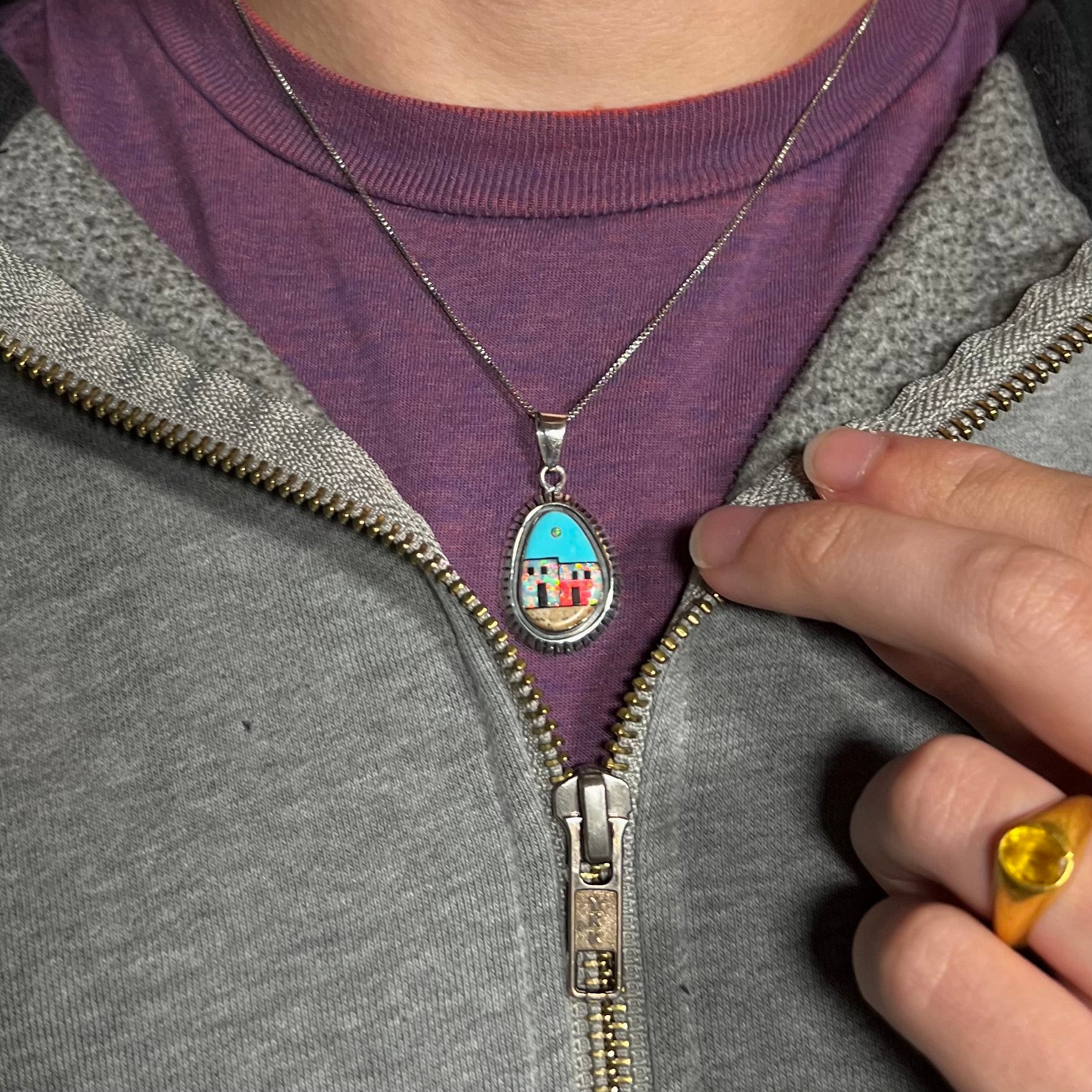 A Southwest-style opal and turquoise inlay necklace worn around a man's neck against a purple shirt.