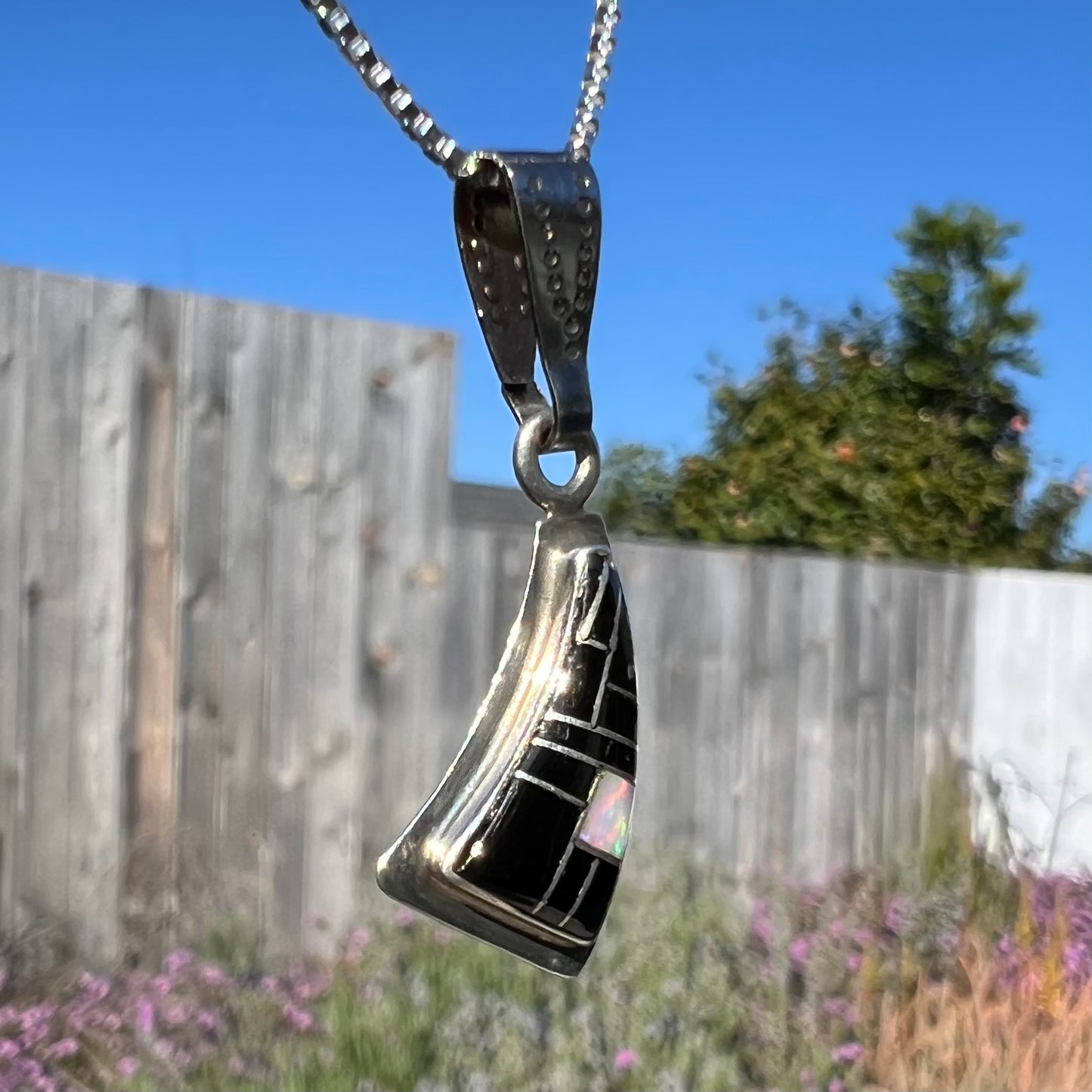 Opposite angled side view of Southwest-style silver opal and onyx inlay necklace outside, showing opal color play in natural light.