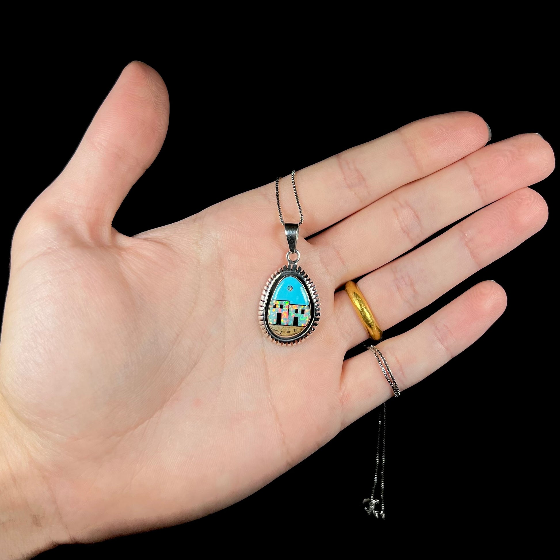 A Southwest-style silver opal and turquoise inlay necklace, held in a hand against a black background.