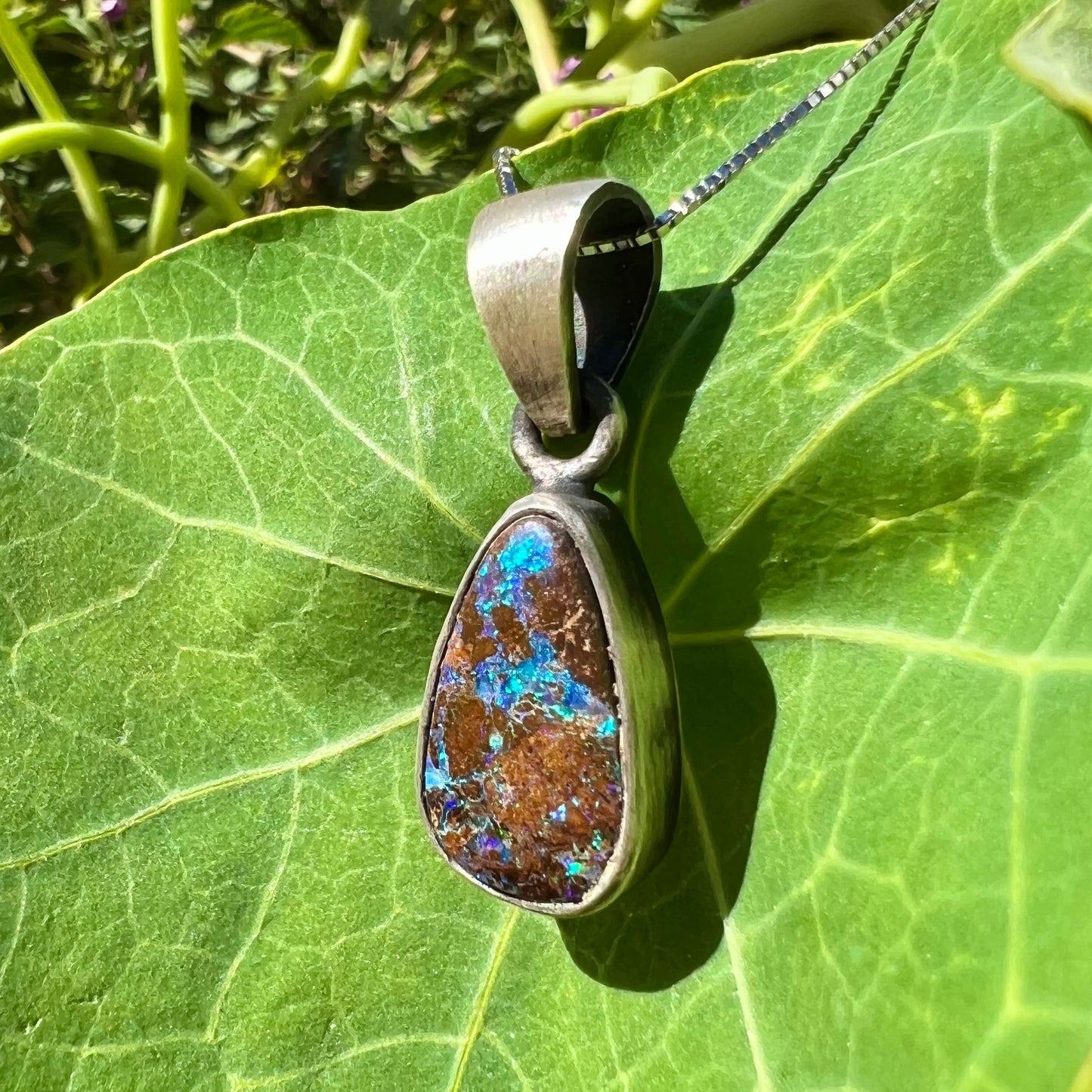 A handmade, satin finish sterling silver pendant set with a drop shaped boulder opal stone.