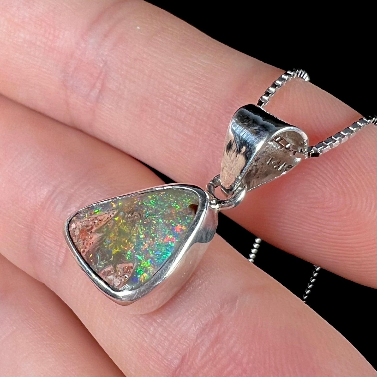 A sterling silver boulder opal necklace on a box chain. The opal twinkles bright red, green, and blue colors.
