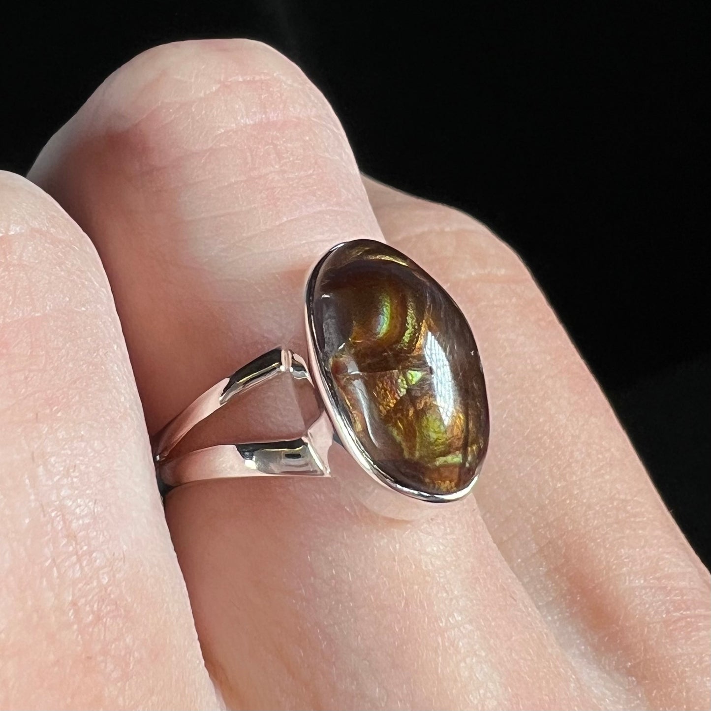 Angled close-up of a sterling silver Mexican fire agate ring with a split shank on a finger.
