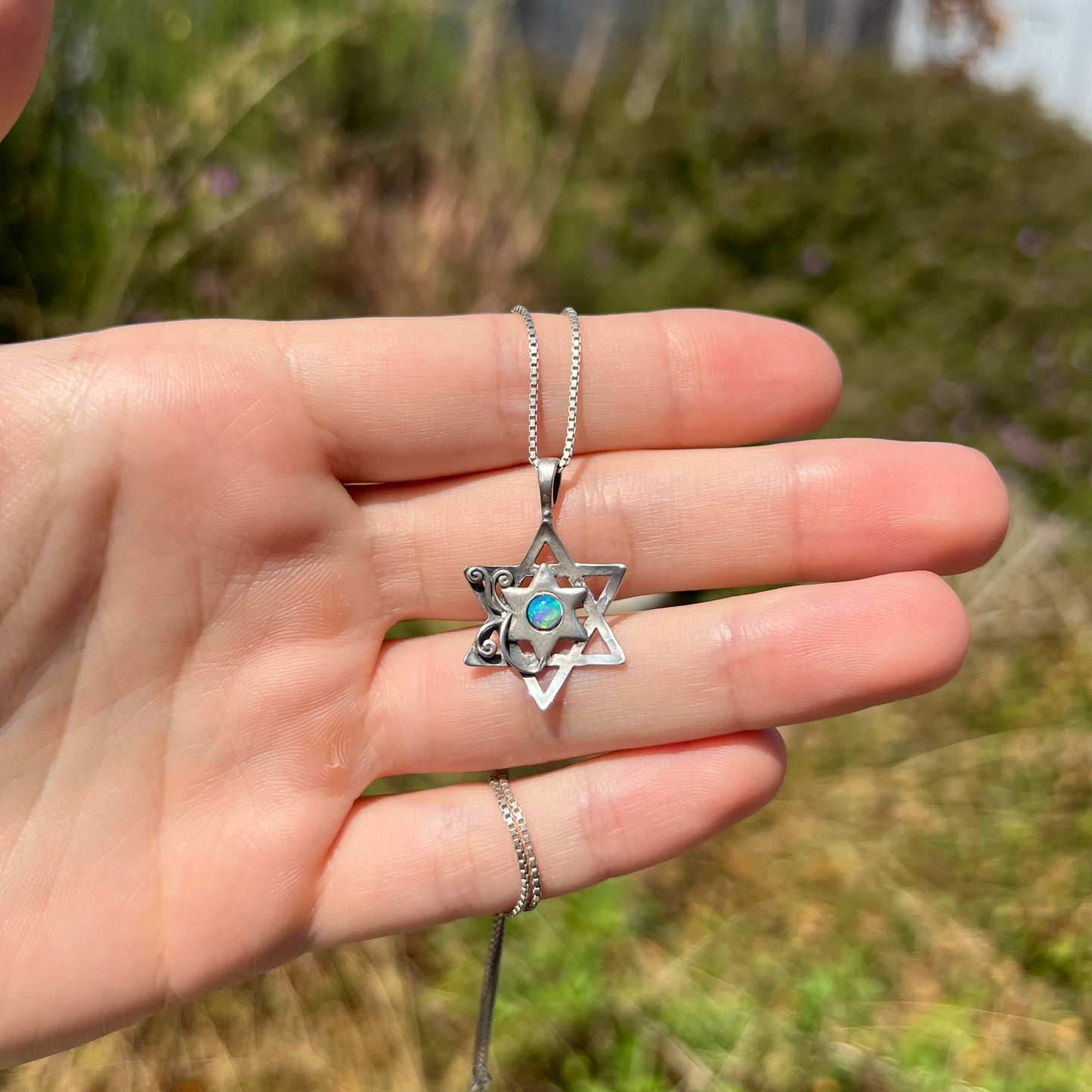 A sterling silver Star of David necklace set with a round blue lab-created opal shown in the sunlight.