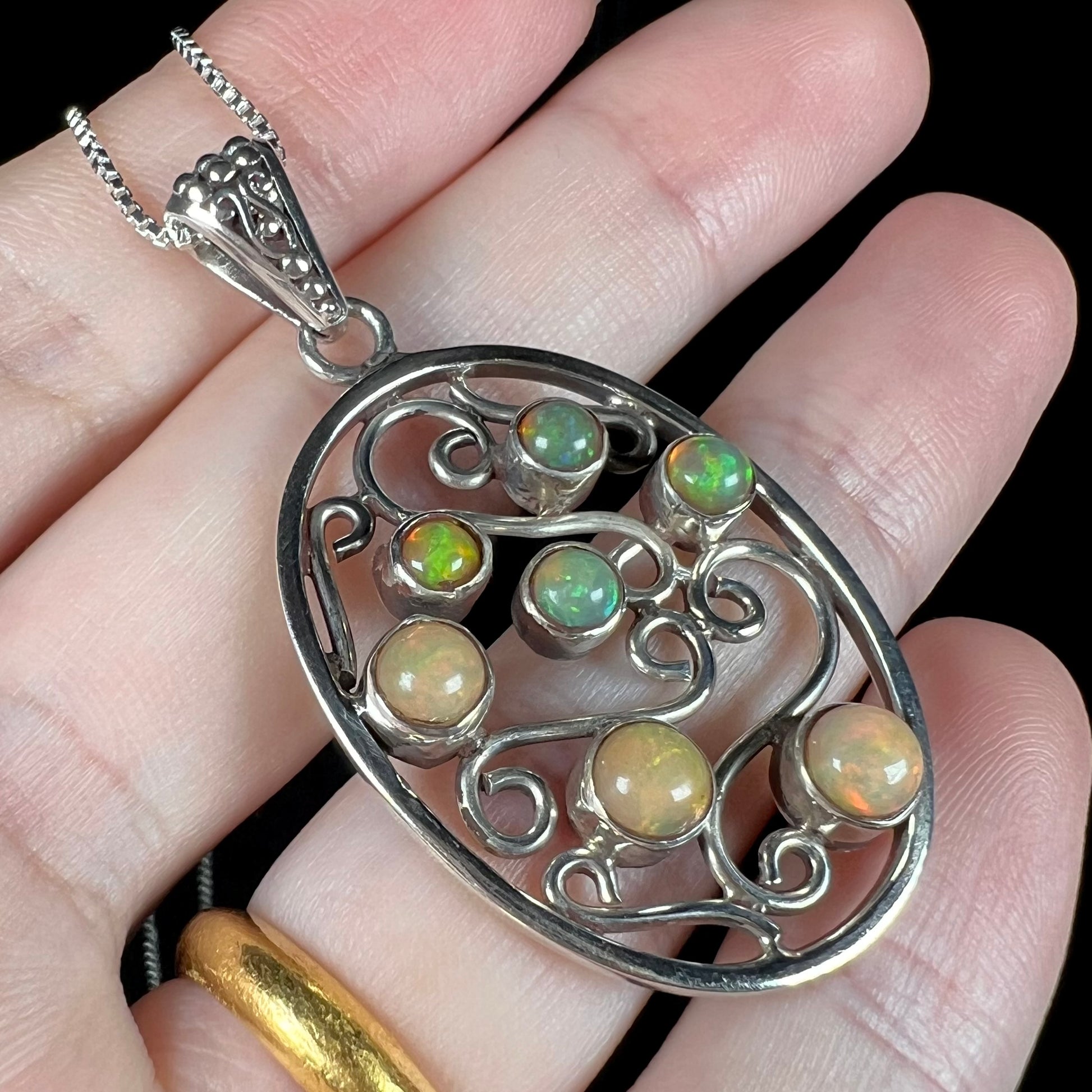 A sterling silver Ethiopian opal filigree necklace, shown at an angle in a hand against black background.