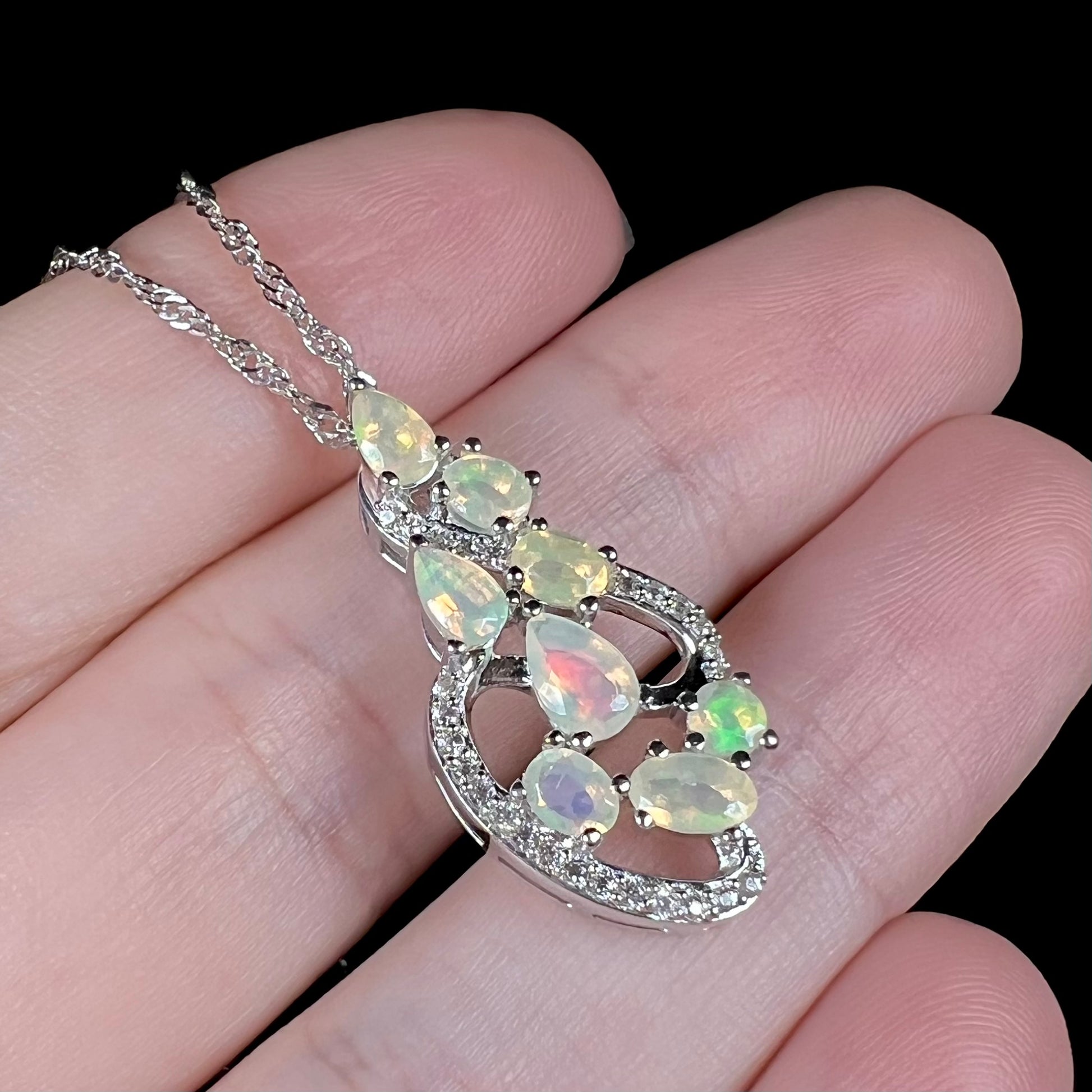 A sterling silver Ethiopian opal and CZ necklace, held at an angle.  The opals have red, green, and purple colors.