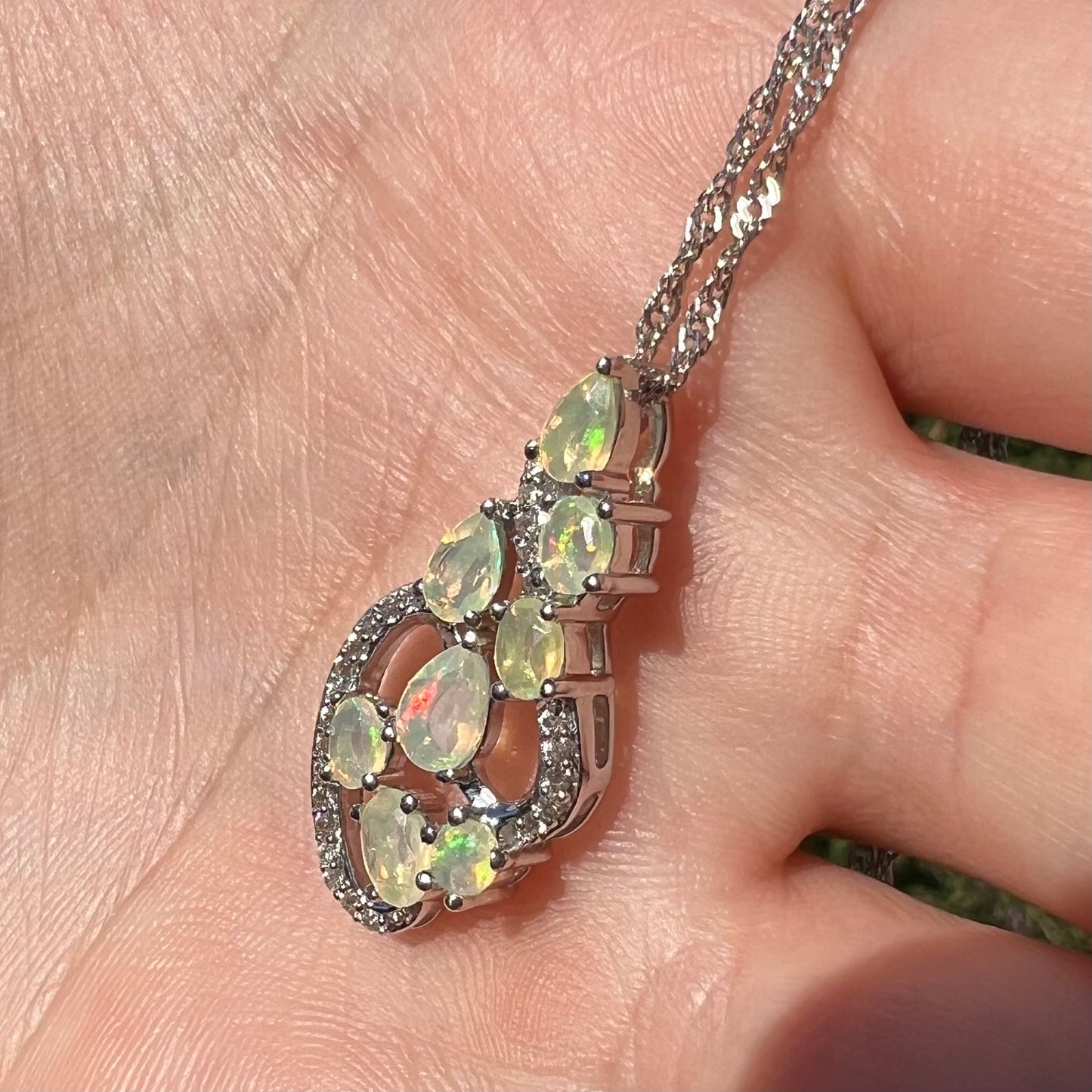 A sterling silver Ethiopian opal necklace shown at an angle in a hand, lit by natural sunlight.