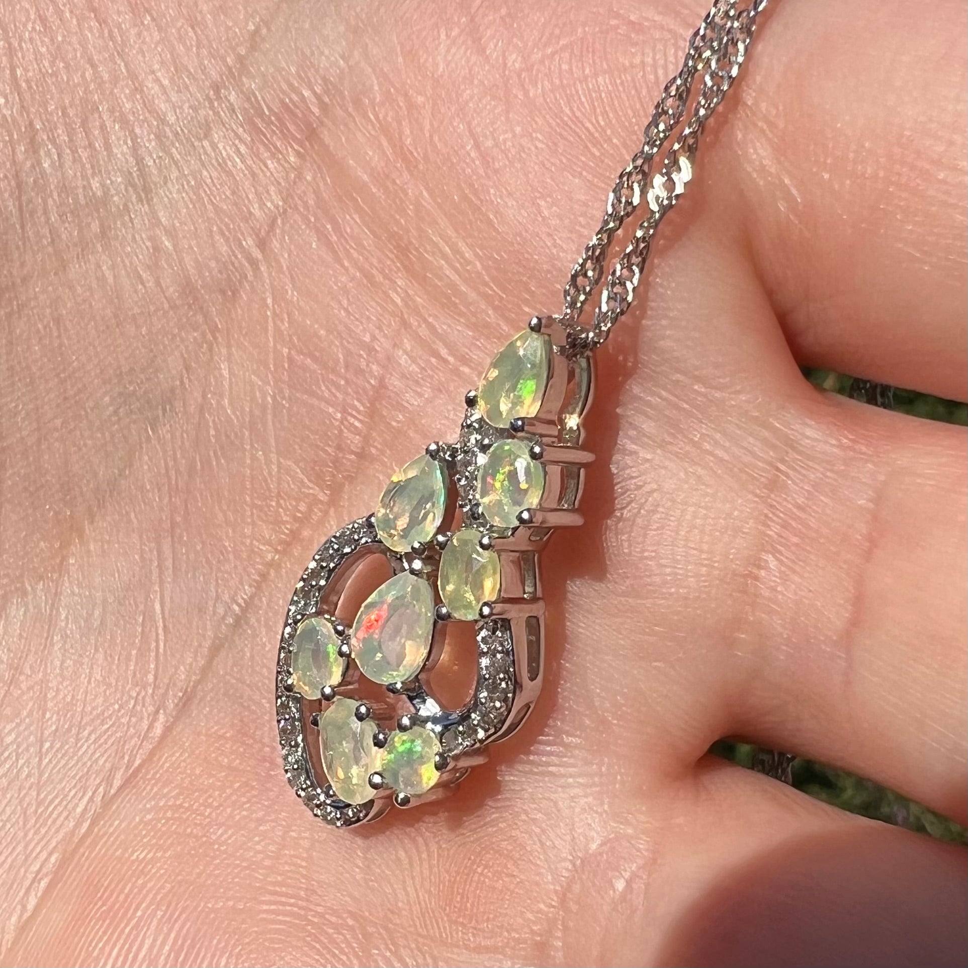 A sterling silver Ethiopian opal necklace shown at an angle in a hand, lit by natural sunlight.