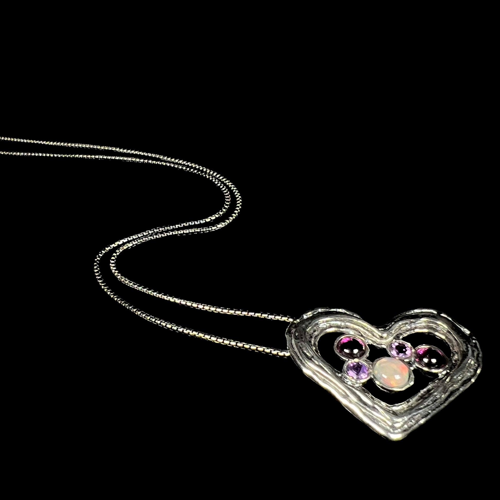A sterling silver heart necklace set with a round Ethiopoian opal, two amethysts, and two rhodolite garnets.