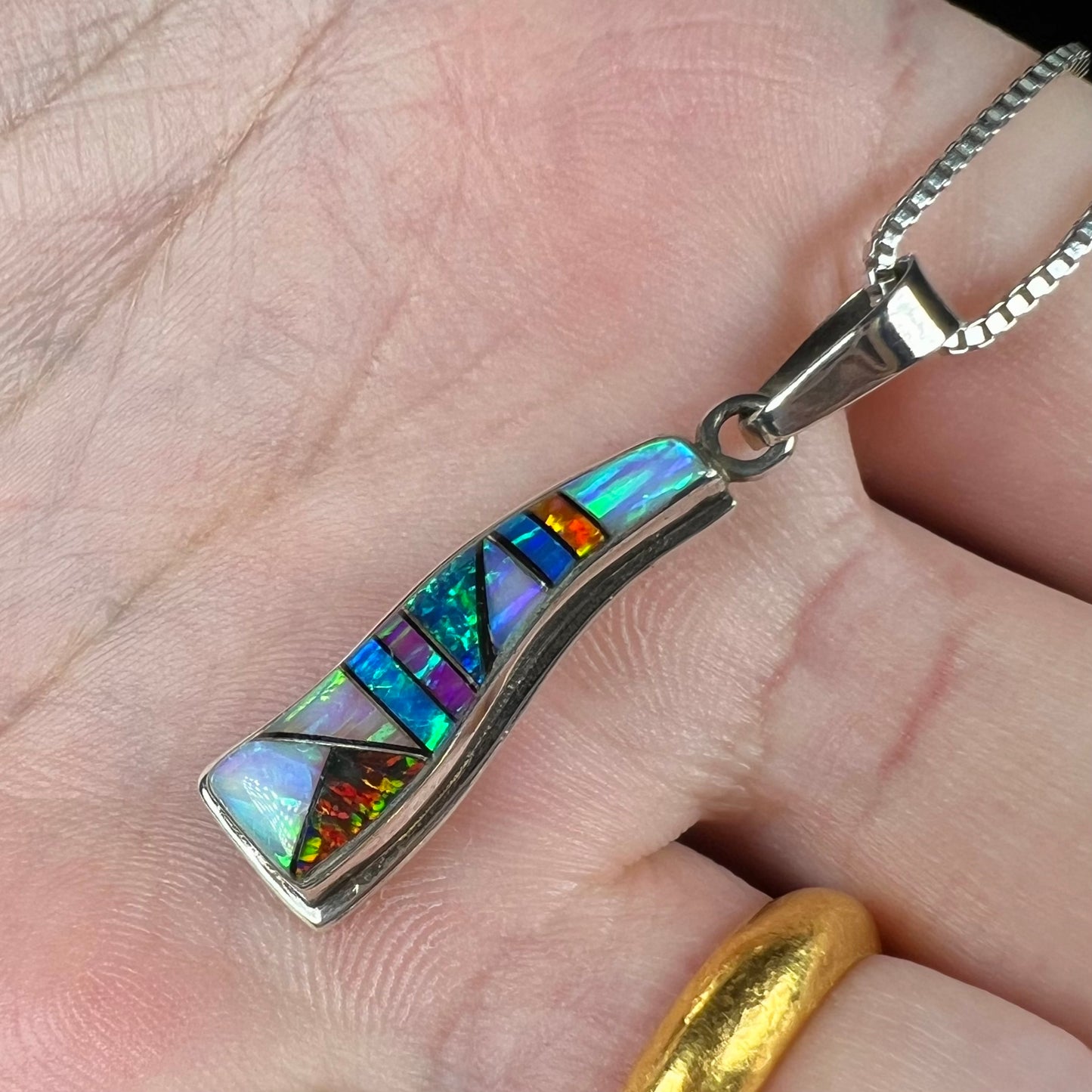 A sterling silver multicolor opal inlay pendant, shown at an angle in a hand close-up.
