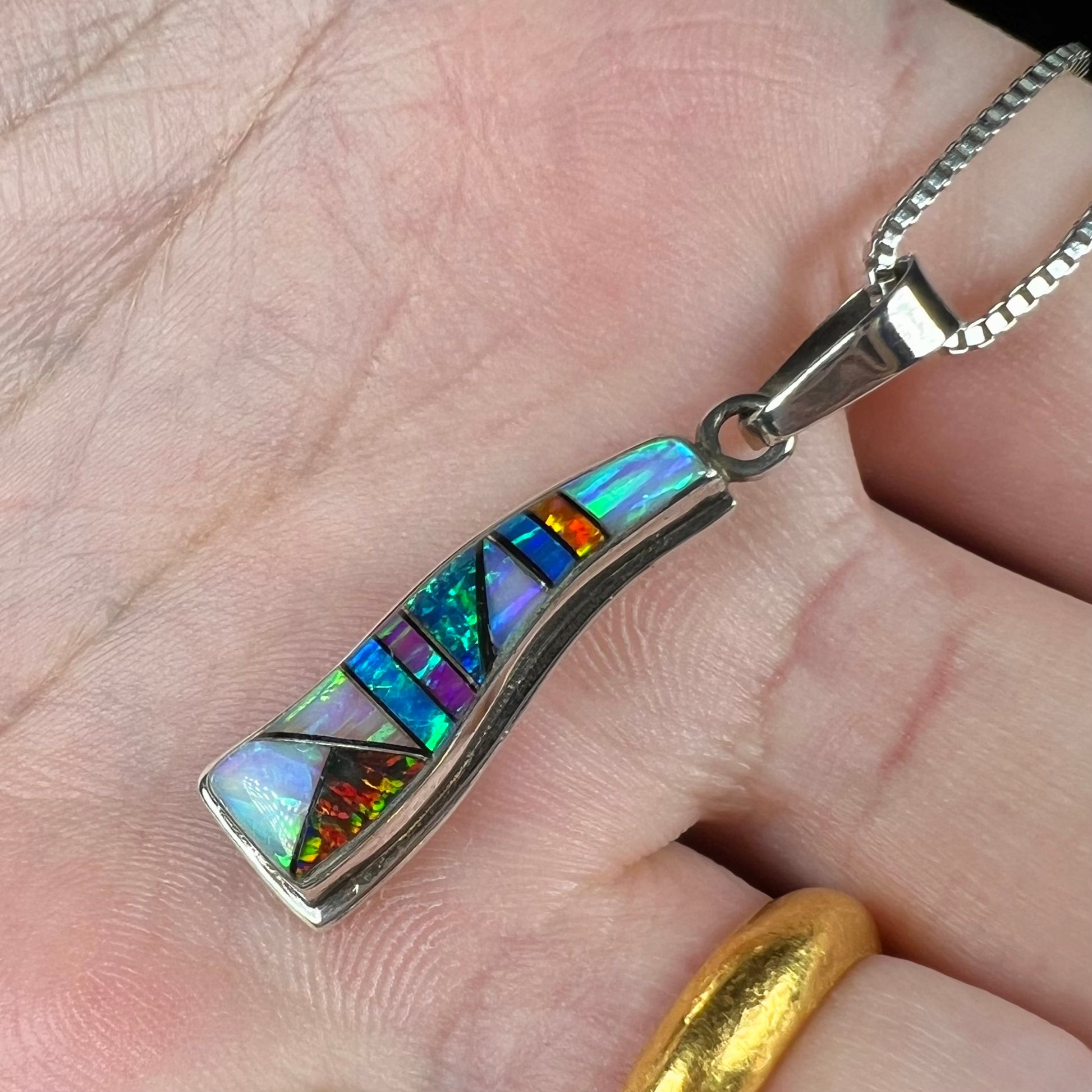 A sterling silver multicolor opal inlay pendant, shown at an angle in a hand close-up.