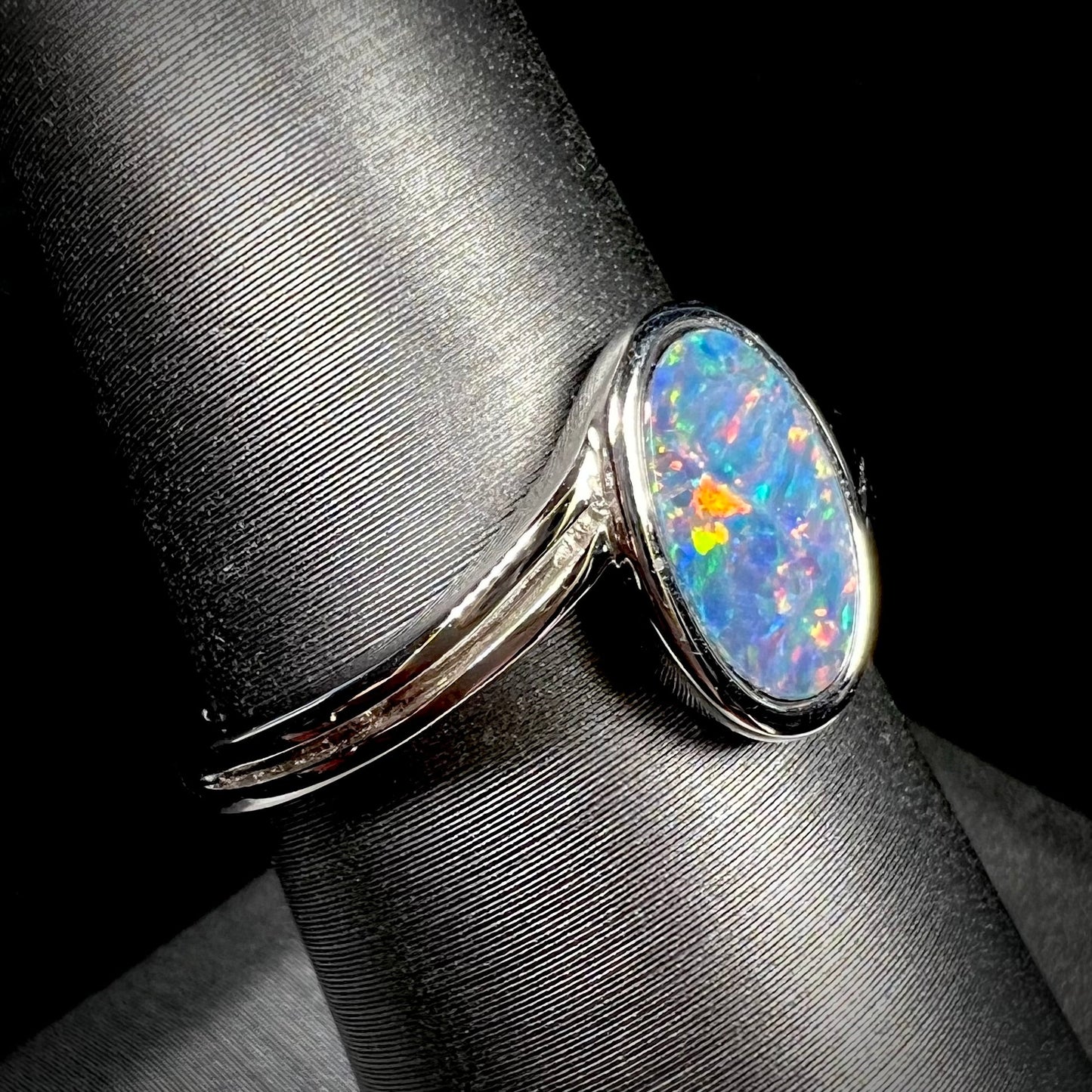 A sterling silver ring bezel-set with an oval shaped black opal doublet. The opal has red and blue fire.