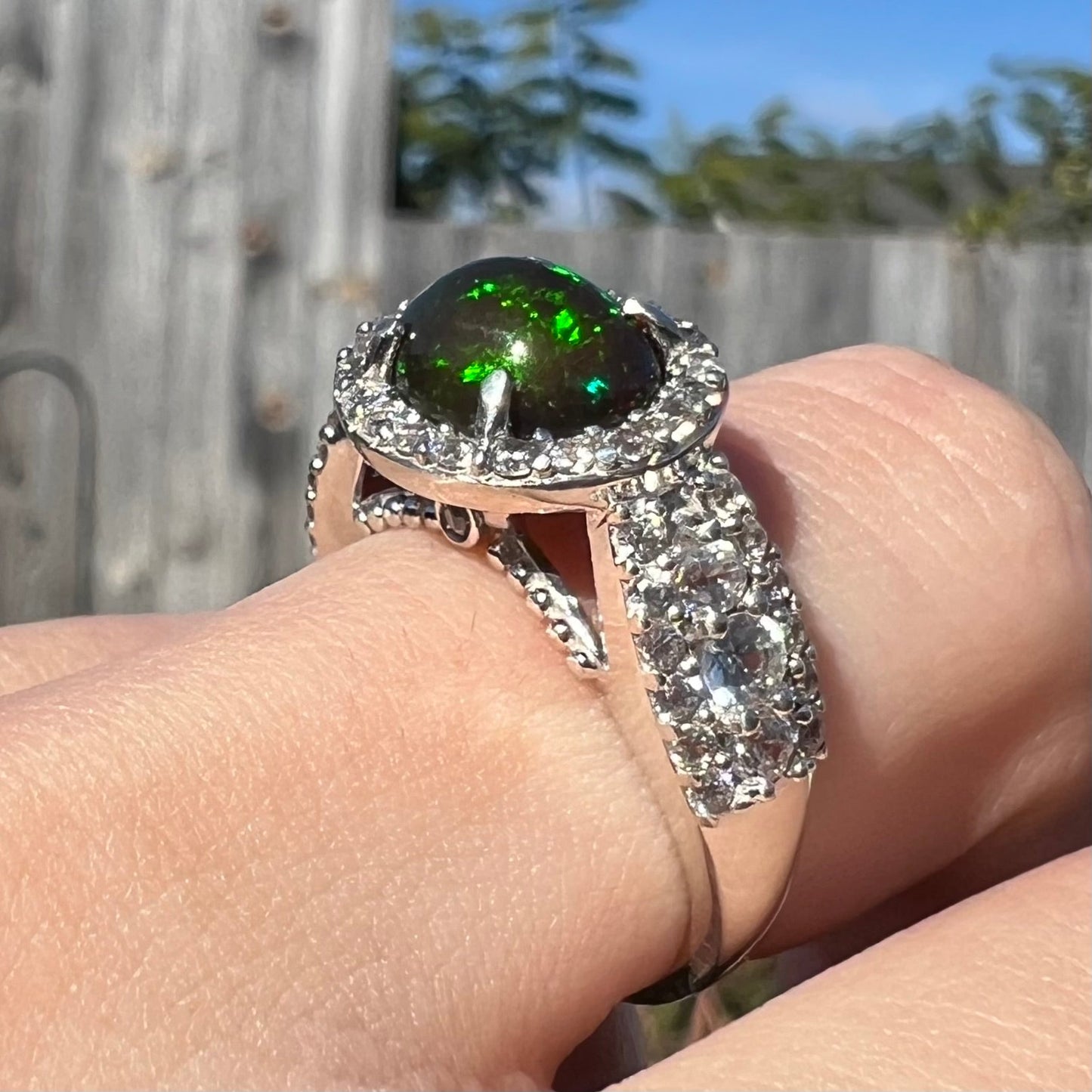 A CZ-accented sterling silver halo ring mounted with a smoked Ethiopian fire opal. The opal plays green, red, and blue colors.