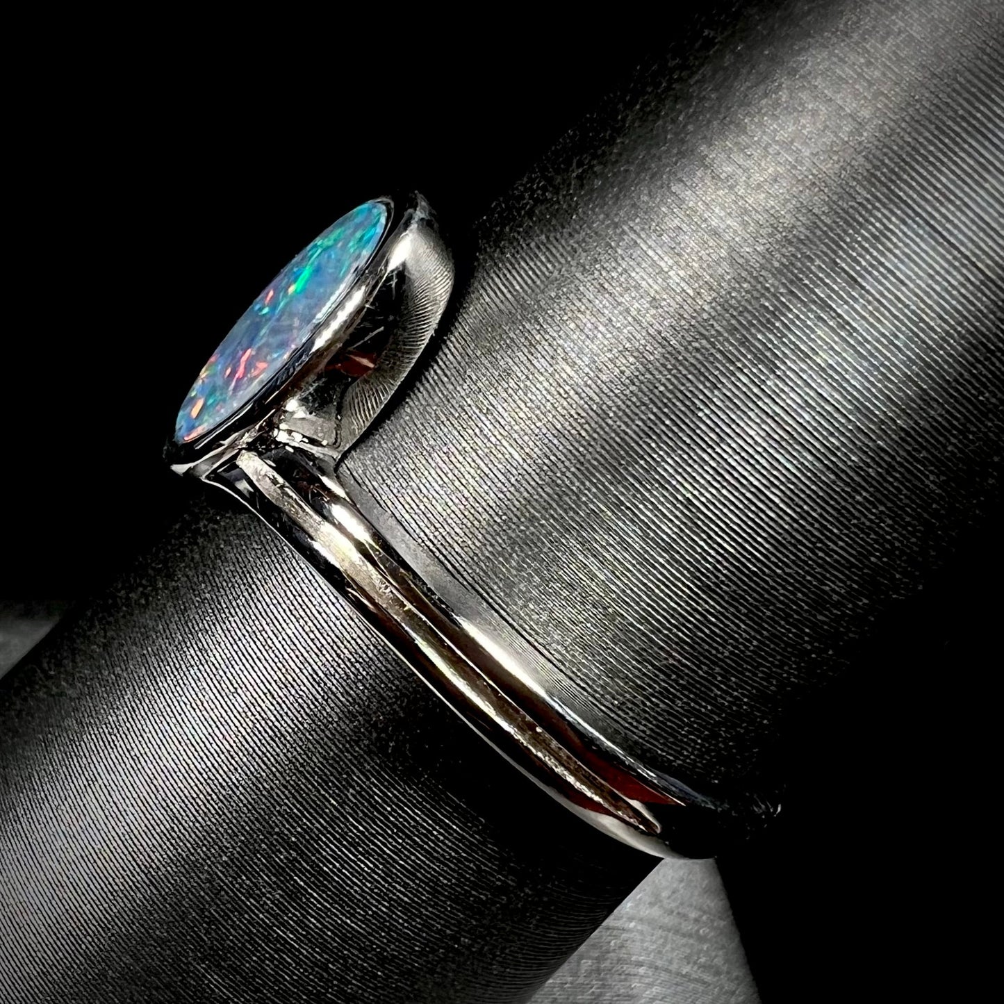 A sterling silver ring bezel-set with an oval shaped black opal doublet. The opal has red and blue fire.