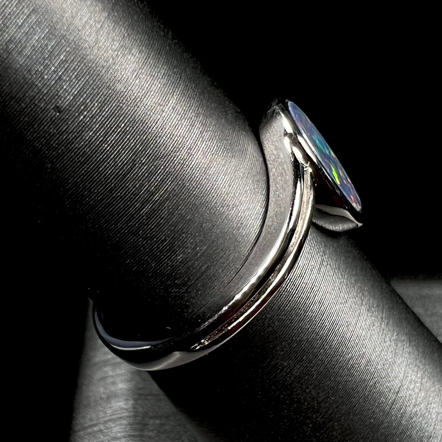 A sterling silver ring bezel-set with an oval shaped black opal doublet. The opal has red and blue fire.