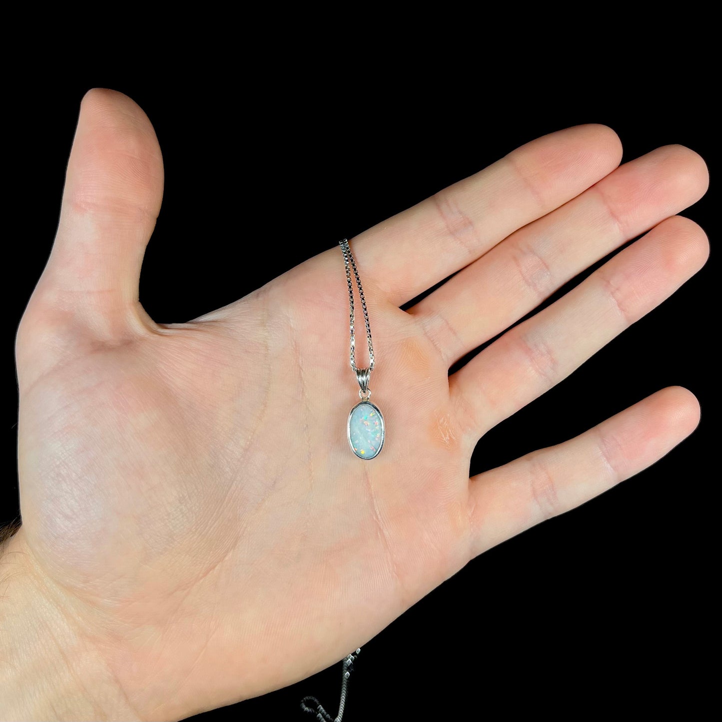 A ladies' sterling silver necklace bezel set with a natural white crystal opal. The opal has red and blue fire.