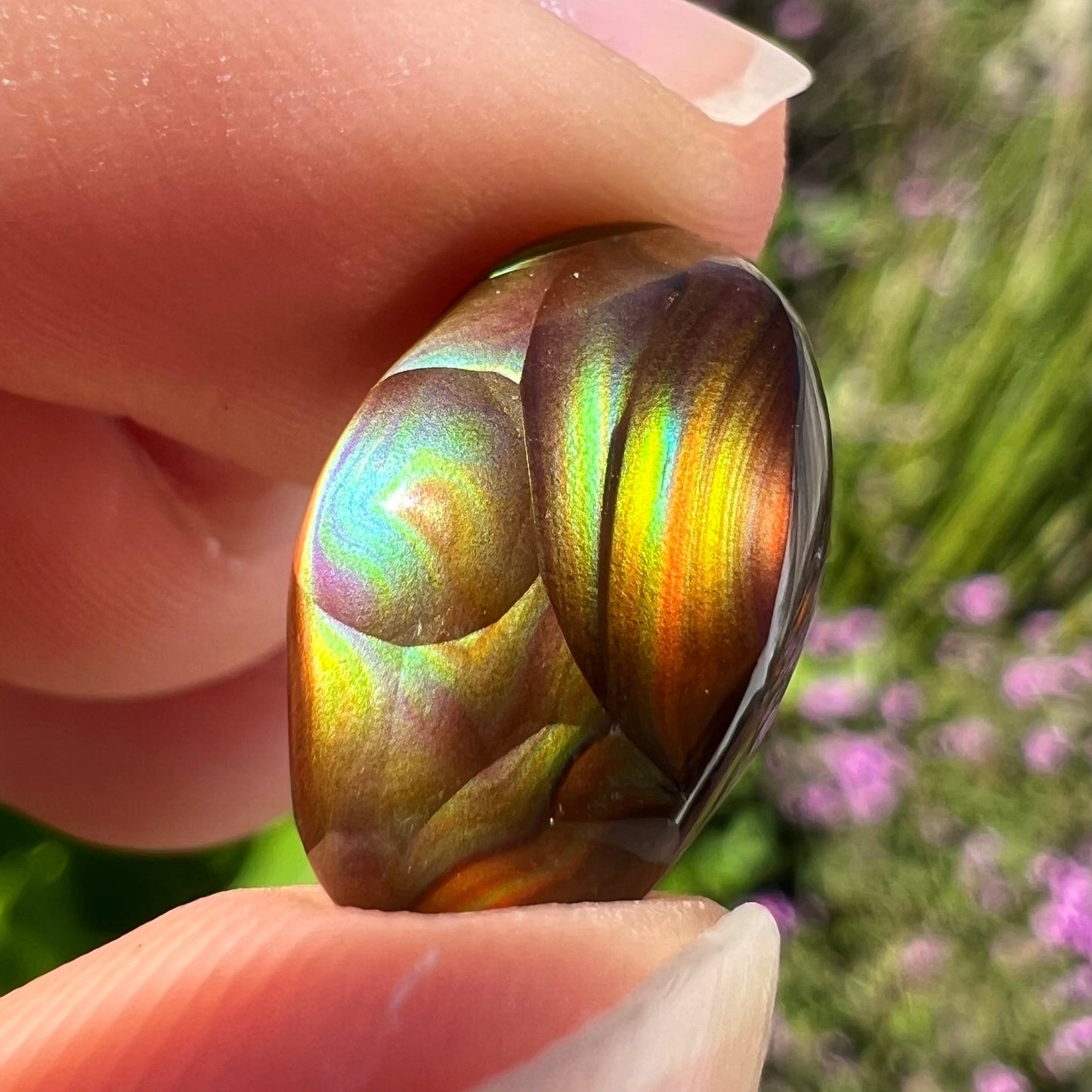 An oval cabochon cut Mexican fire agate stone.  The stone has bright, multicolored iridescent banding.