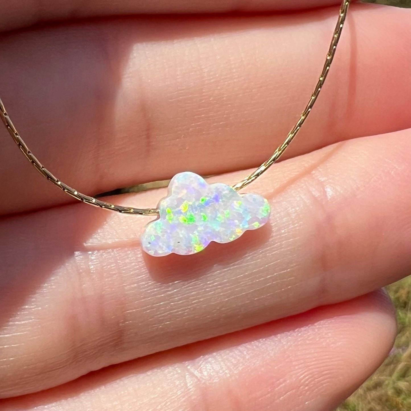 A synthetic opal cloud necklace held at an angle by a hand in natural light.